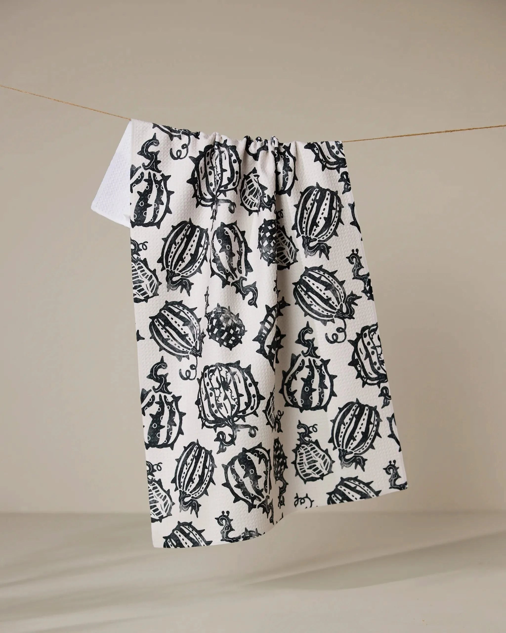 The Geometry Punk Pumpkins kitchen towel, featuring a bold pumpkin pattern and made from recycled materials, hangs on a simple string against a neutral background.