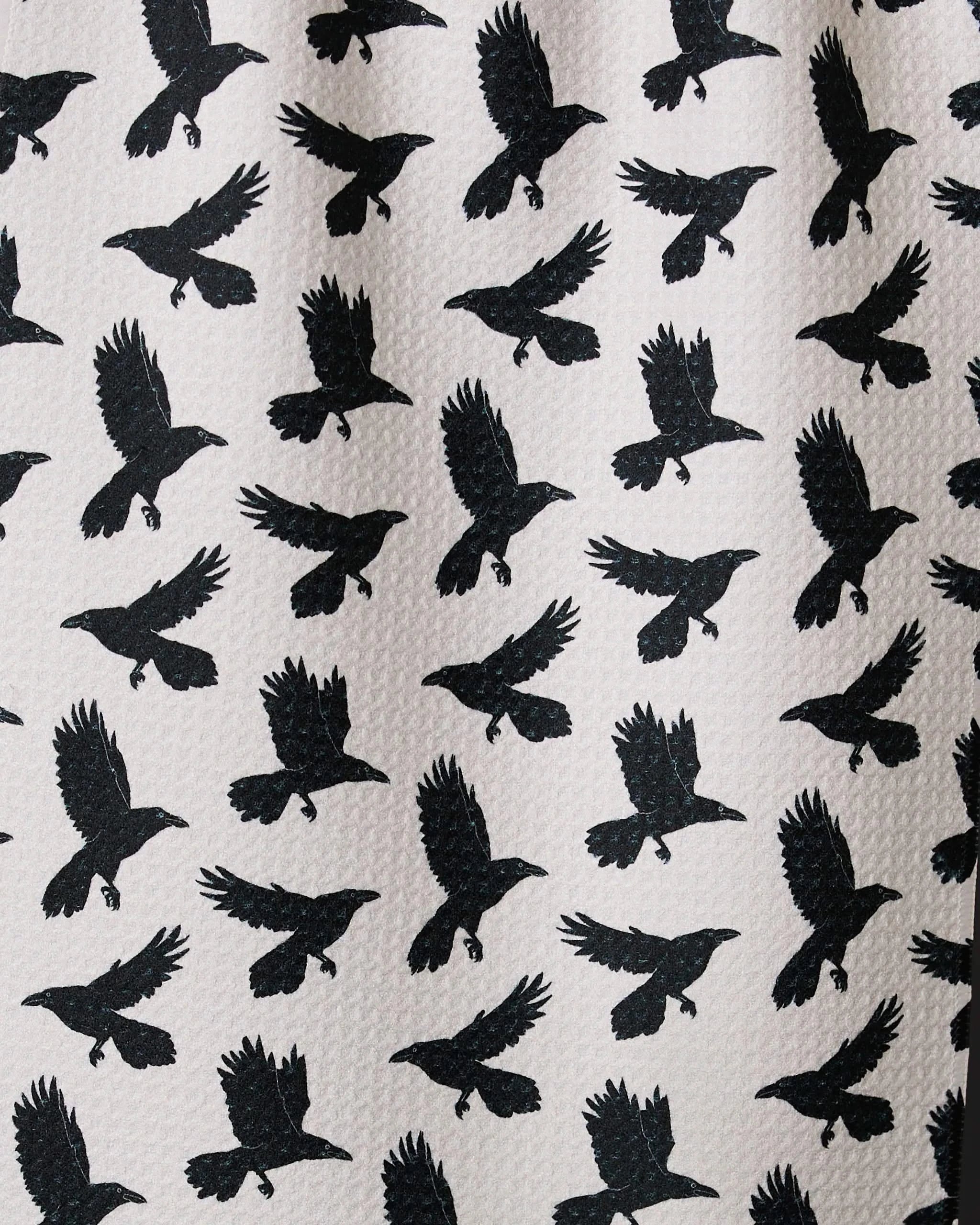 Crow Call by Geometry: a recycled bar towel with a repeating pattern of black birds in flight on a light beige background, their varied wing positions adding dynamic energy to the design.