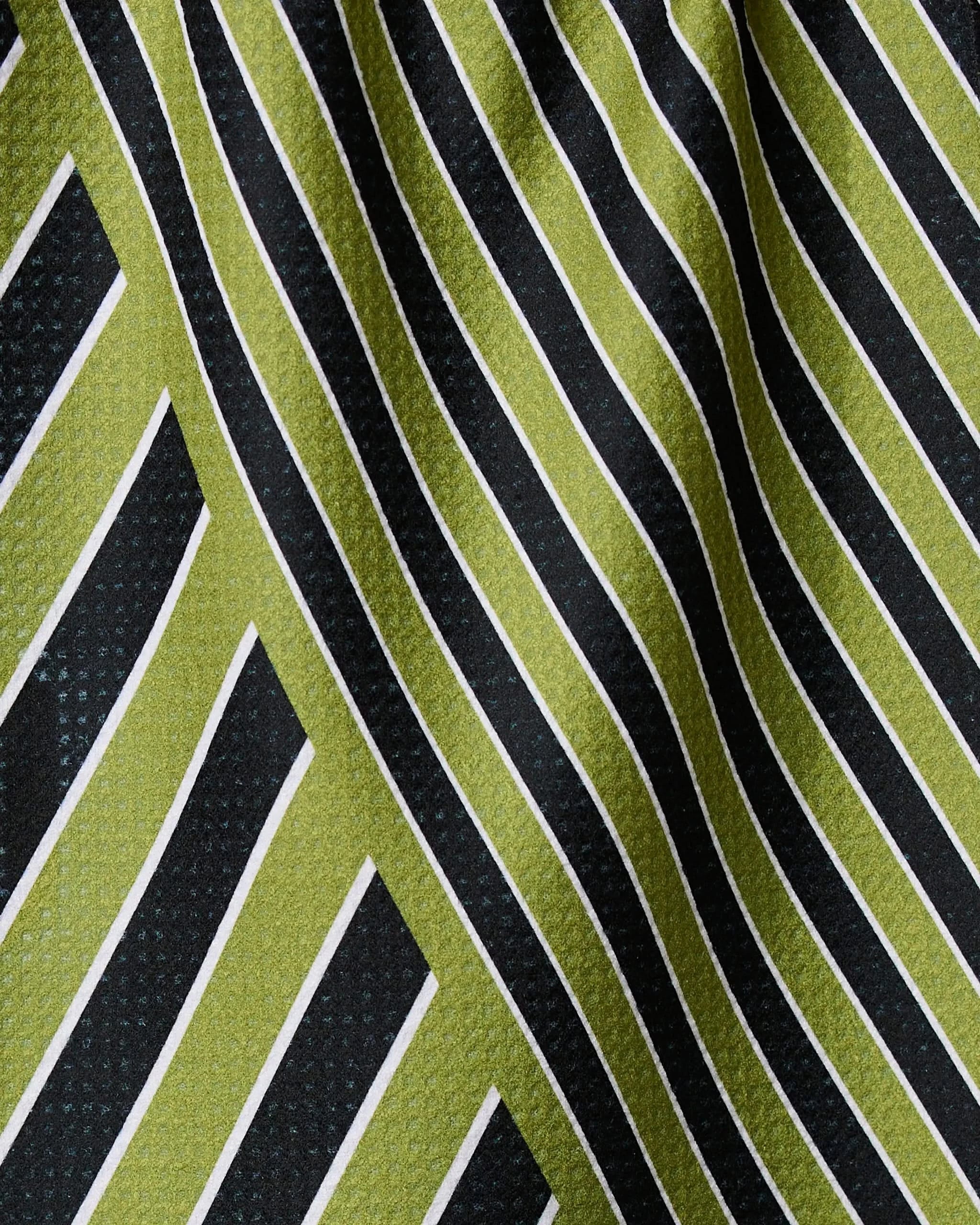 Close-up of Geometry’s Tricky Lines recycled kitchen towel, featuring a geometric pattern with black, olive green, and thin white diagonal stripes on slightly wrinkled fabric for added texture.