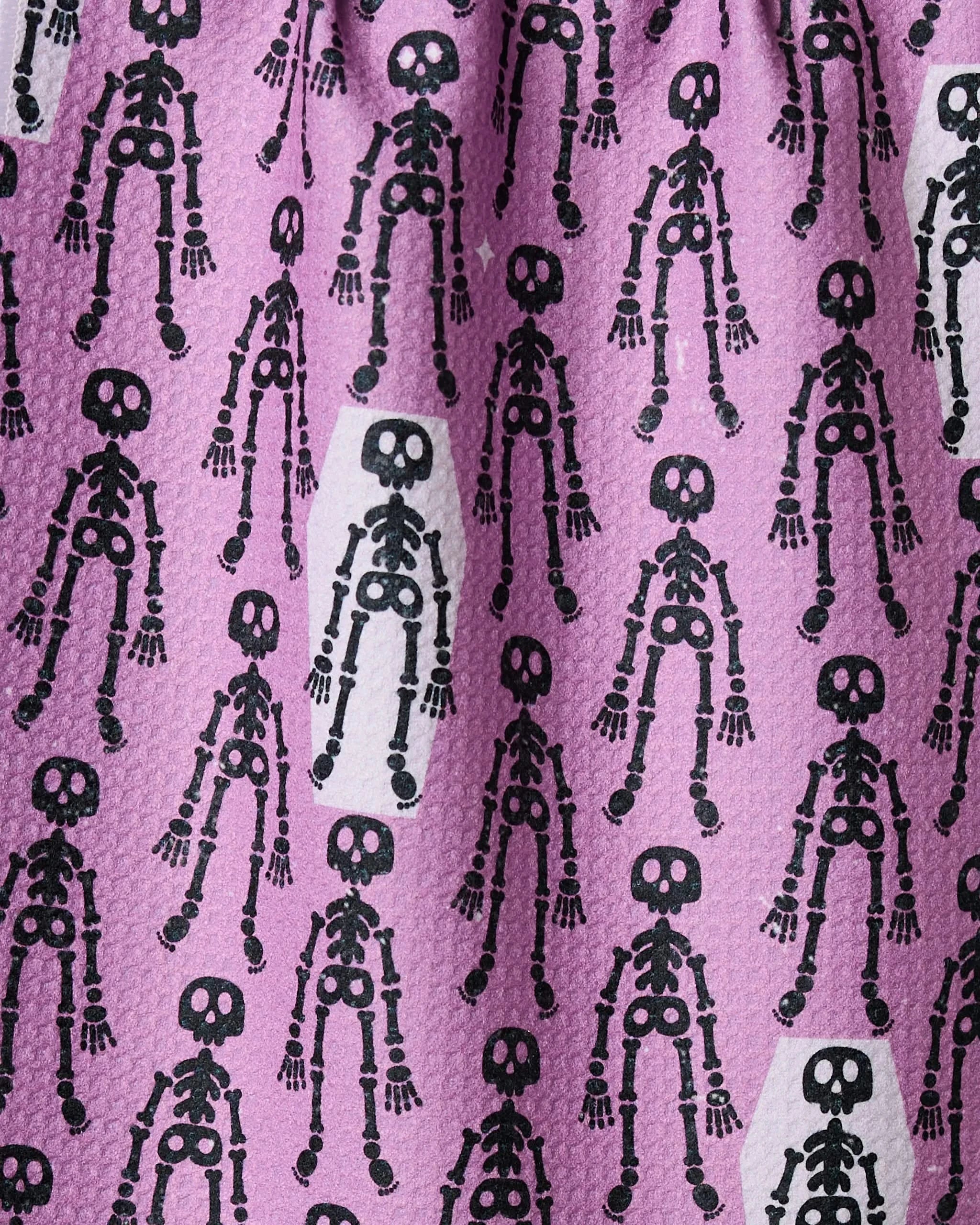 The Geometry Bones and Beds bar towel features a quirky purple fabric with black skeletons, some on white backgrounds, in an ultra-absorbent design made from recycled materials—perfect for adding bold style to your bar.