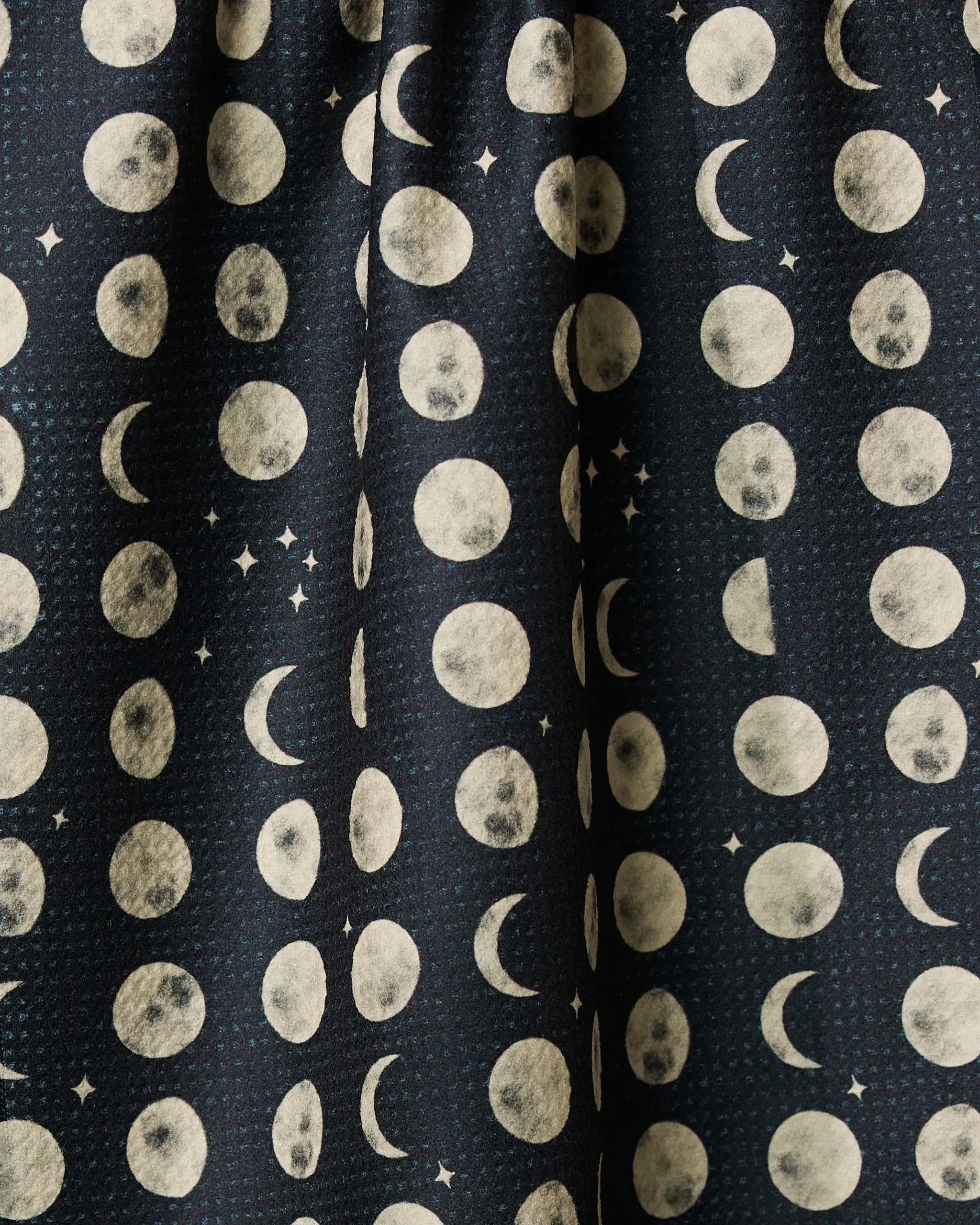 Moon Dots by Geometry is a dark, ultra-absorbent tea towel featuring rows of white moon phases—crescents, halves, full moons—and small stars on a navy blue background.
