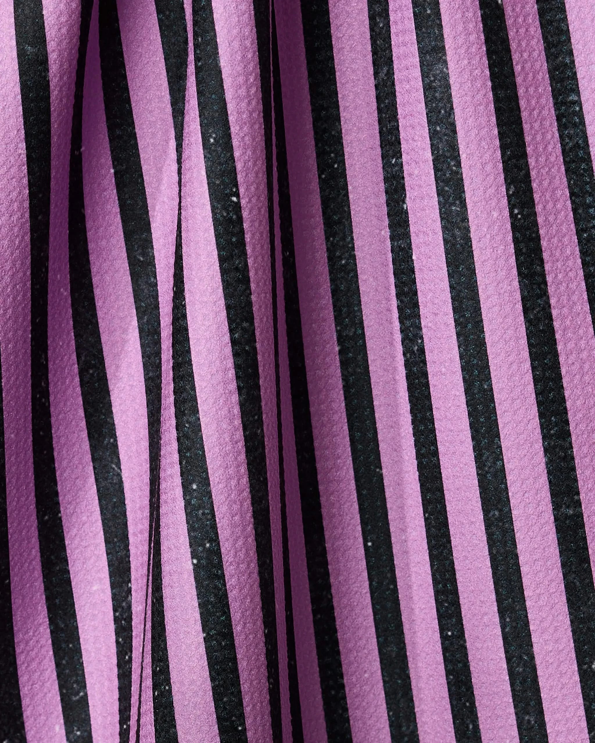 Close-up of Geometry’s Neon Halloween Nights tea towel, featuring ultra-absorbent fabric with vertical black and purple stripes, folds forming shadows and curved lines.