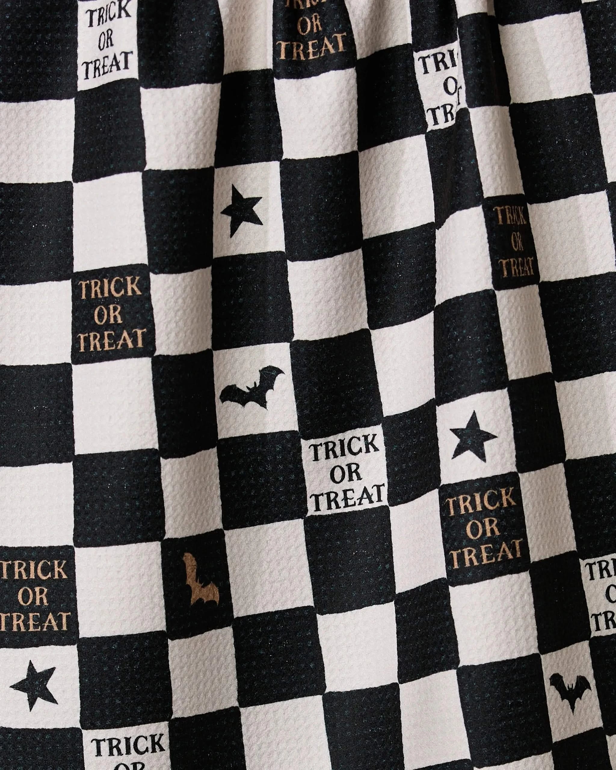 Geometrys Tricks and Treats tea towel features a black and white checkered pattern with Halloween designs—TRICK OR TREAT text, stars, bats, and cats. This eco-friendly kitchen towel is perfect for the spooky season.