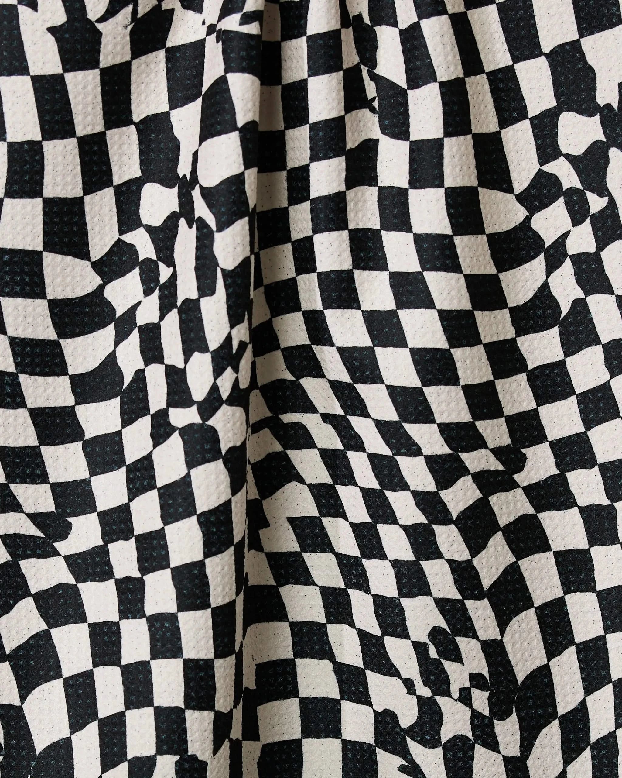 The Geometry Glitchy Check tea towel features a black and white checkered wavy pattern for an optical illusion effect, made from ultra-absorbent, slightly rough fabric for efficient drying.
