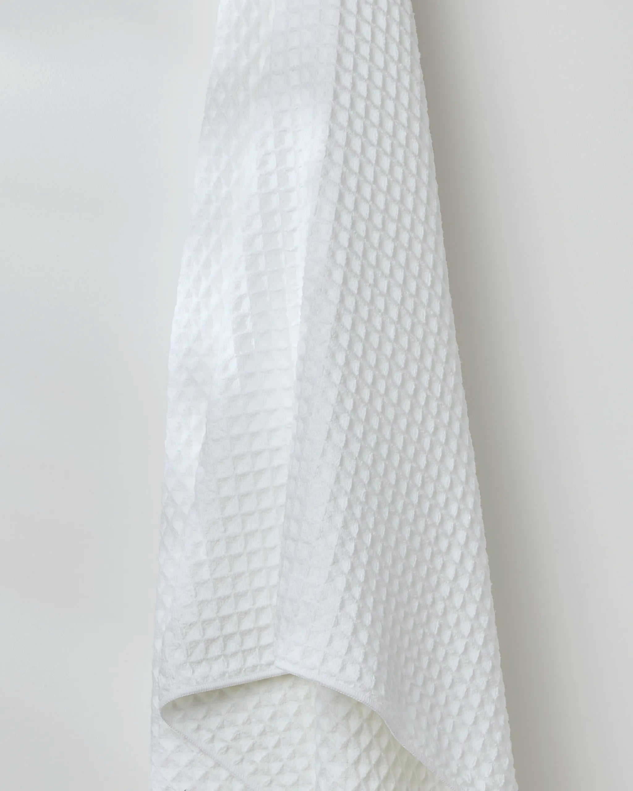 The GEOMETRY Cloud bath towel, featuring a textured waffle pattern, hangs against a plain white wall.