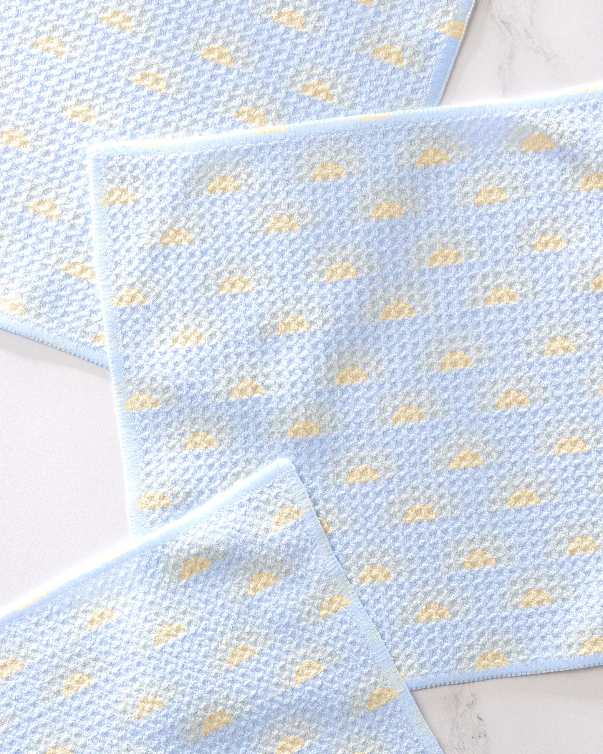 Three light blue GEOMETRY "Soft Summer Sun" dishcloths with a yellow cloud pattern and matching blue borders are neatly arranged on a white surface, showcasing their soft, super-absorbent woven design.