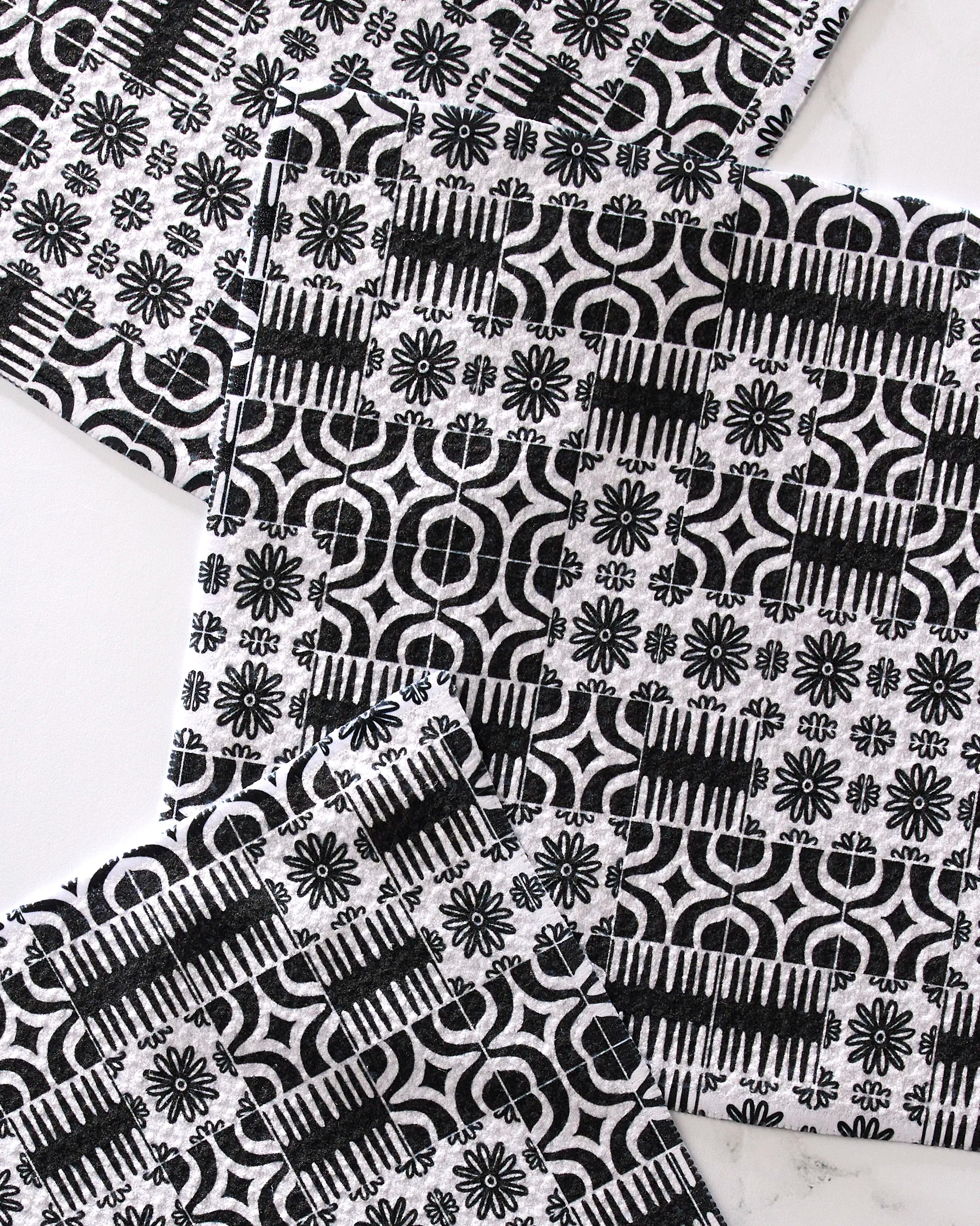 Four Bohemian Mosaic coasters by GEOMETRY, featuring black and white geometric and floral designs on recycled materials, are arranged with overlapping corners on a light surface.