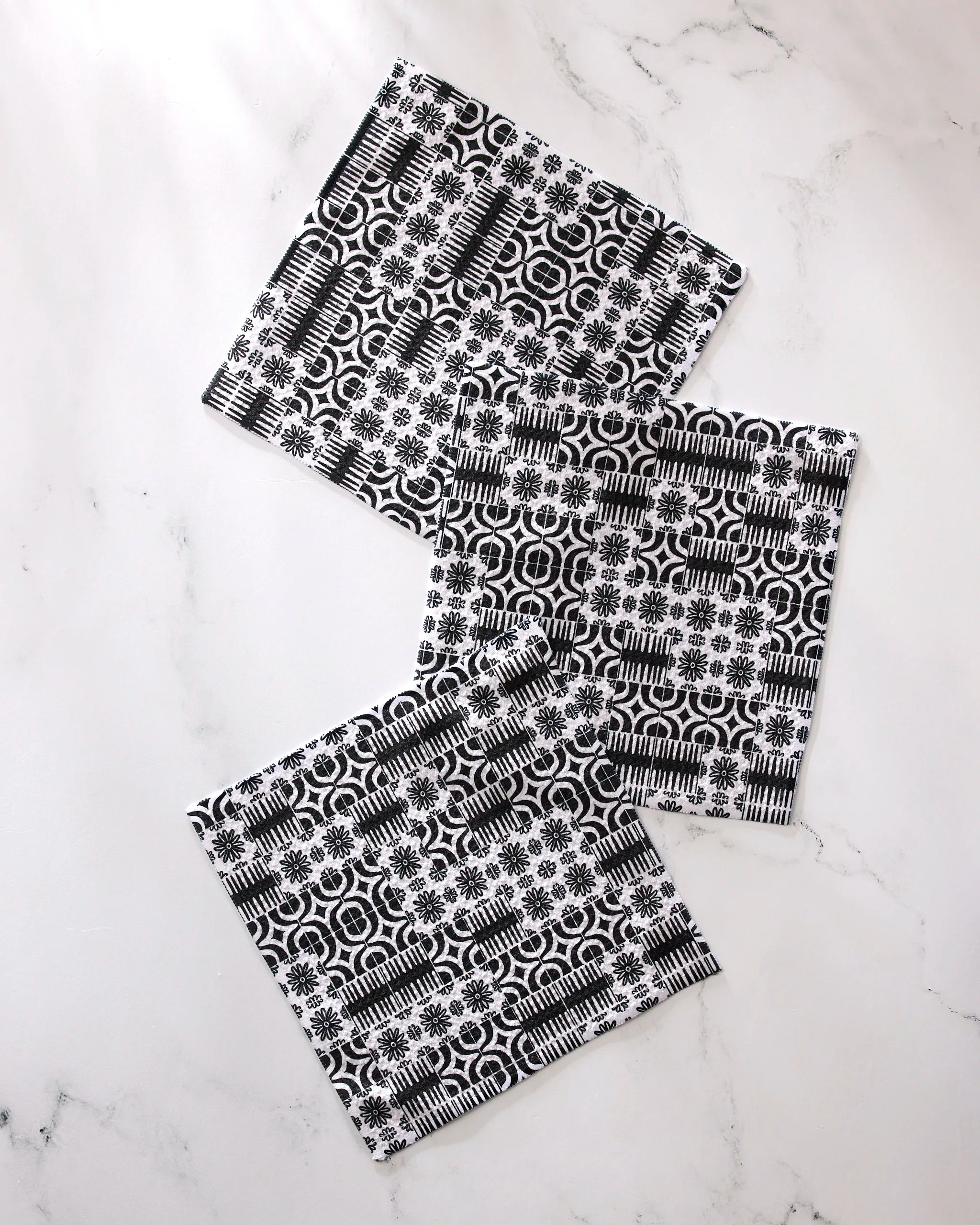 Three super-absorbent GEOMETRY Bohemian Mosaic dishcloths with black and white geometric and floral patterns are displayed on a white marble surface.