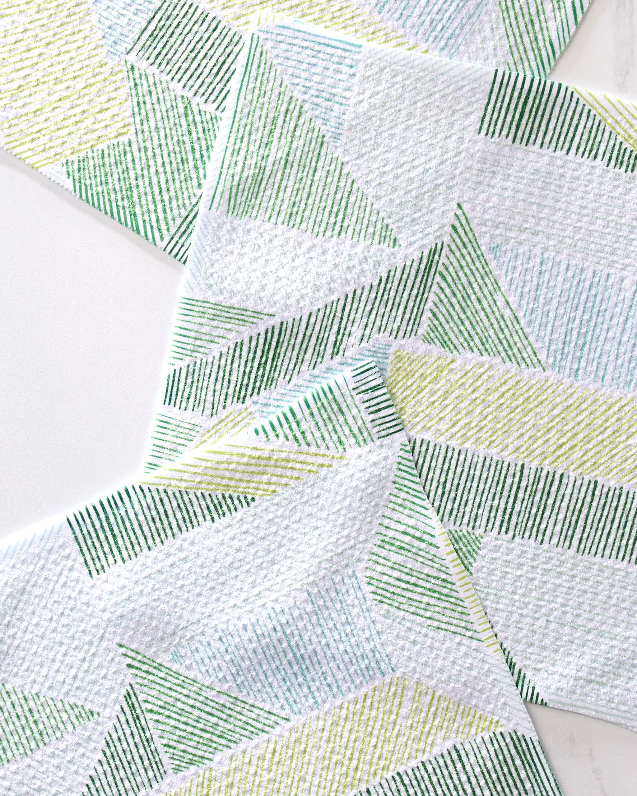 The GEOMETRY "Green Kites" dishtowel set features super-absorbent white towels adorned with green and yellow geometric lines, triangles, and diagonal stripes.