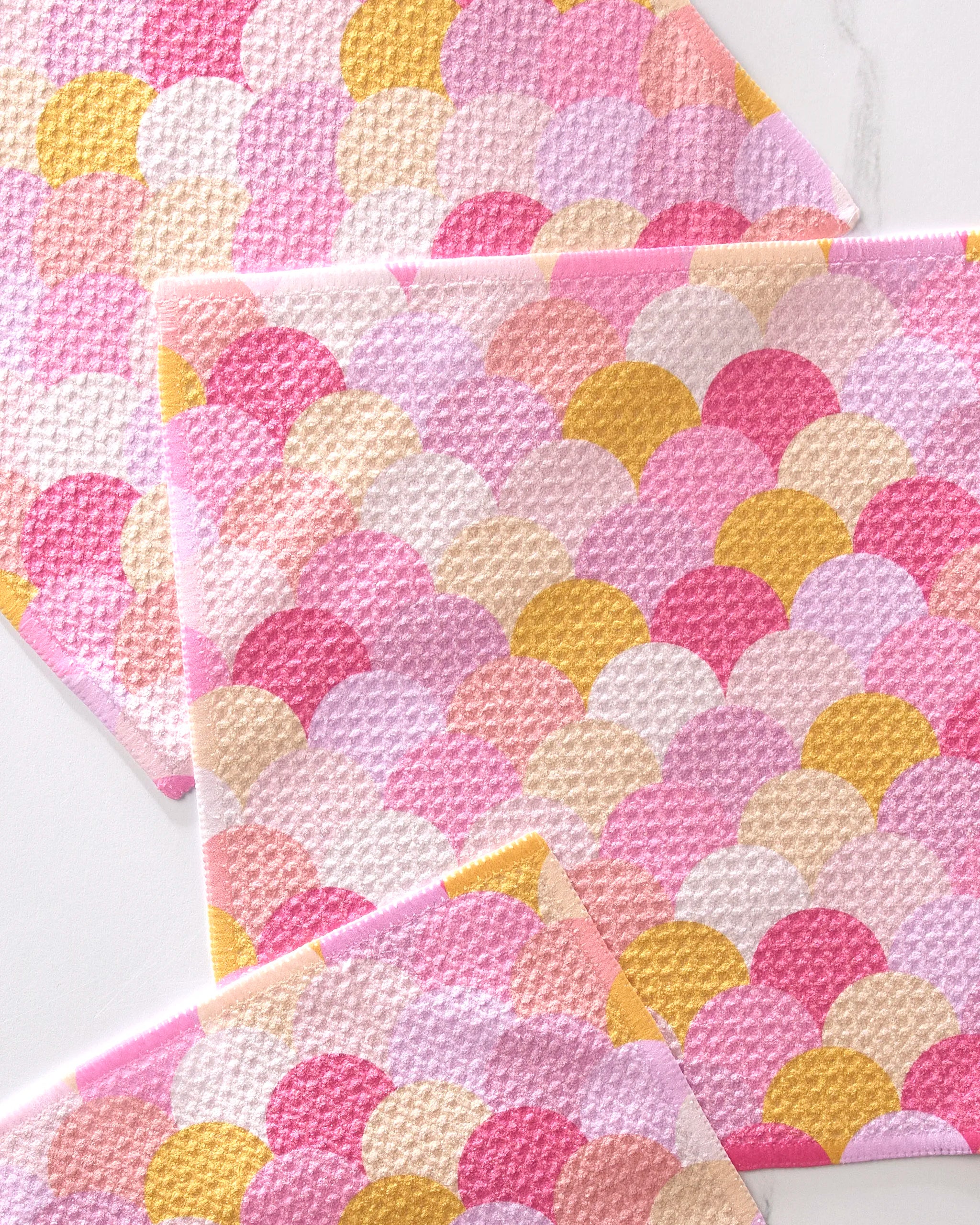 The GEOMETRY Inherit set features three eco-friendly dishcloths with a pink, yellow, and white scallop pattern, crafted from recycled materials and stylishly layered against a white background.