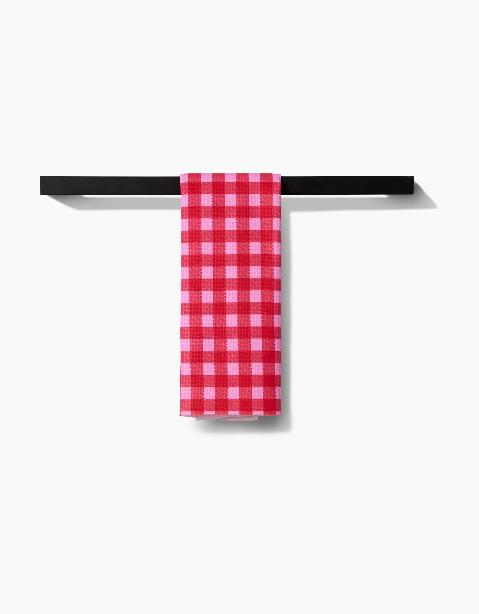 The GEOMETRY Cherry Gingham hand towel hangs neatly on a simple black bar, displaying its ultra-absorbent Geoweave fabric and signature red and white checks against a plain white background.