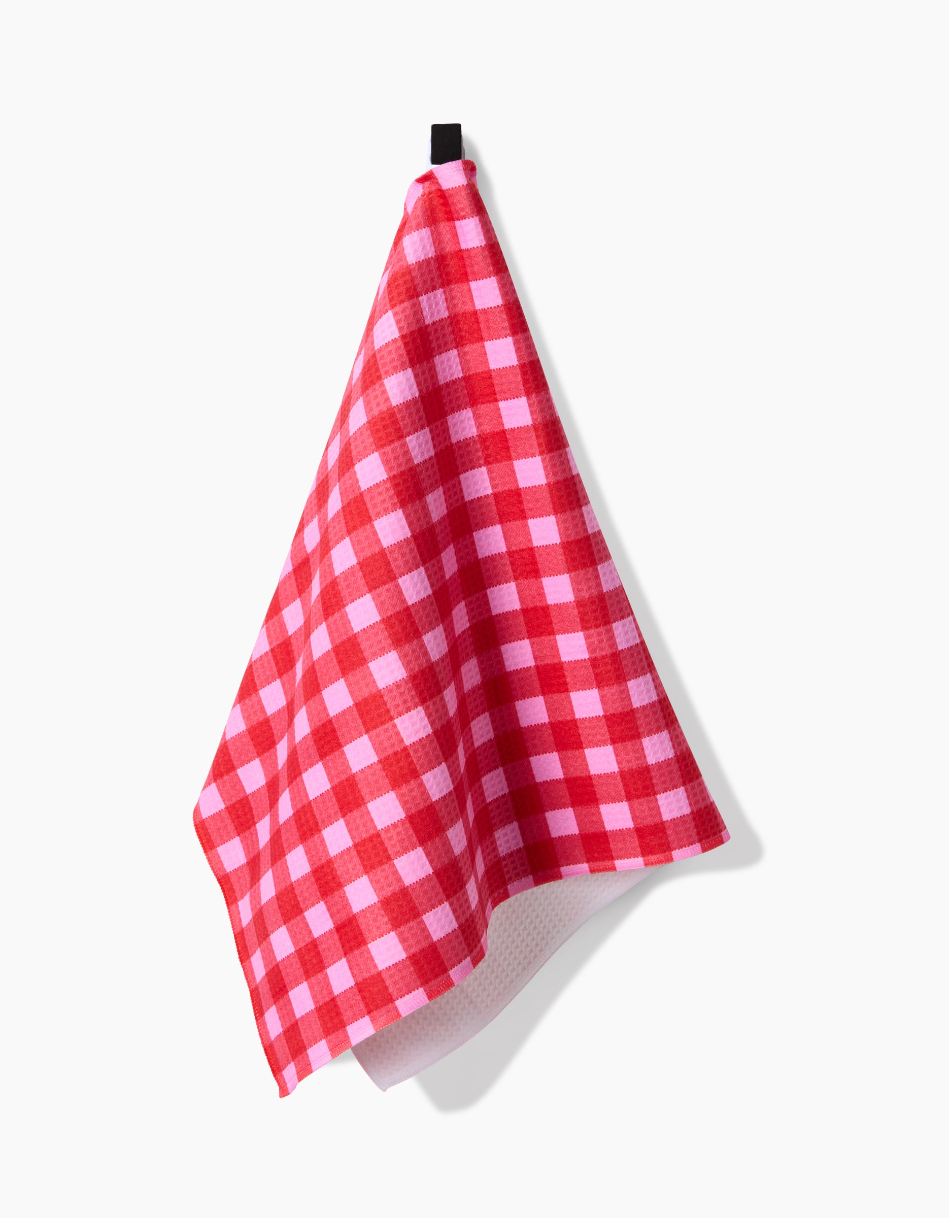 The GEOMETRY Cherry Gingham kitchen towel, featuring ultra-absorbent Geoweave technology, hangs on a black hook against a plain white background.
