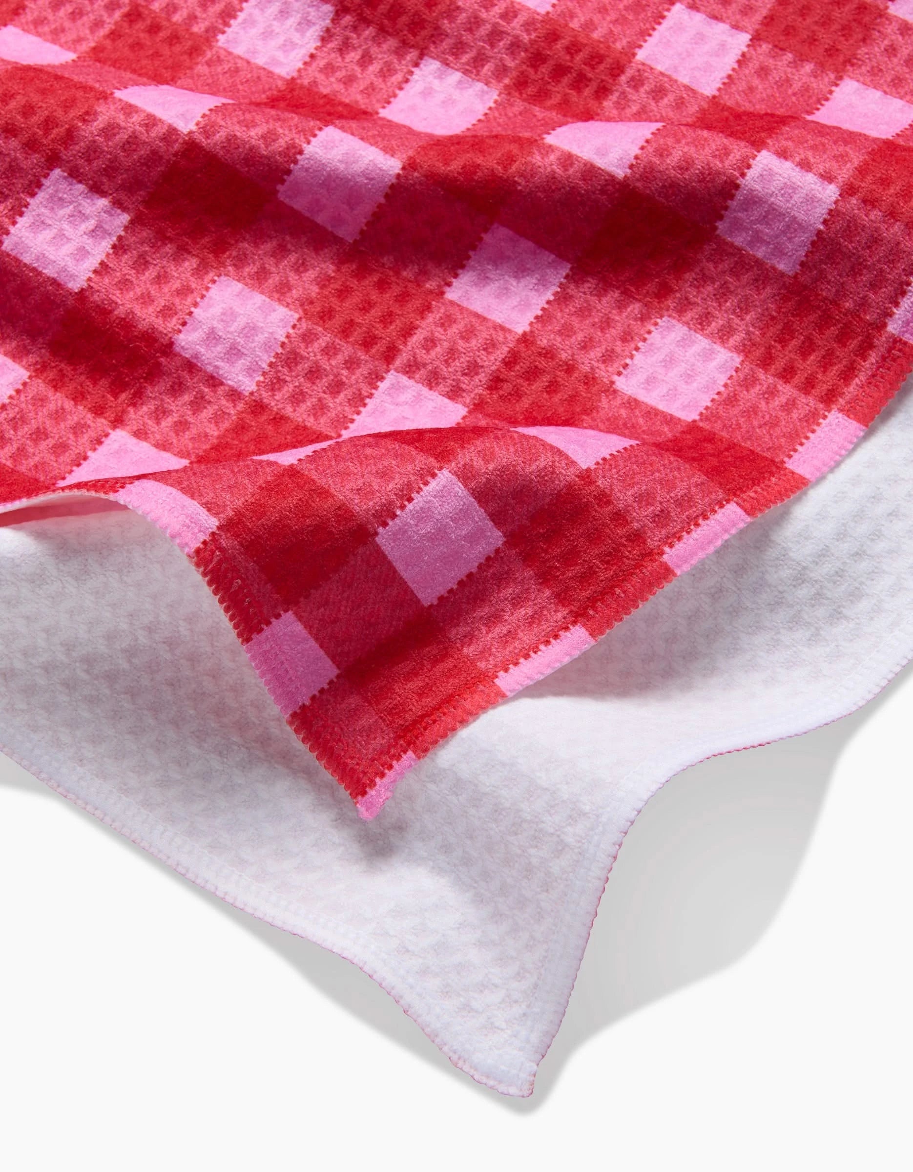 A close-up of the GEOMETRY Cherry Gingham Luxe Hand Towel, featuring a red and pink checkered waffle texture, white back with pink-edged stitching—crafted for ultra-absorbency.