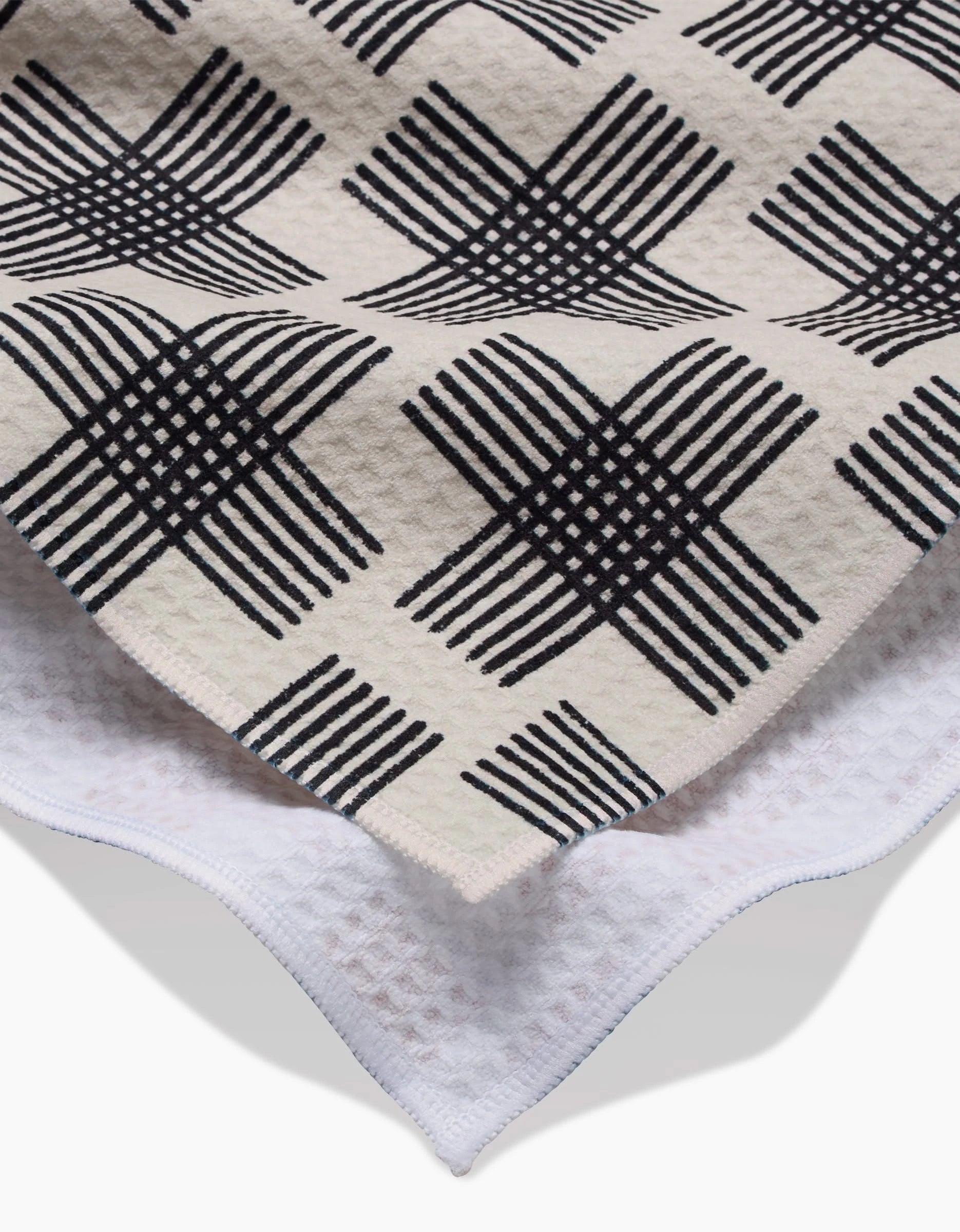 A close-up of Cross Hatch by Rosa Kichline: the beige top layer features a black geometric checkered pattern over a white, waffle-textured base, crafted with Geoweave technology for an ultra-absorbent Luxe Hand Towel finish.
