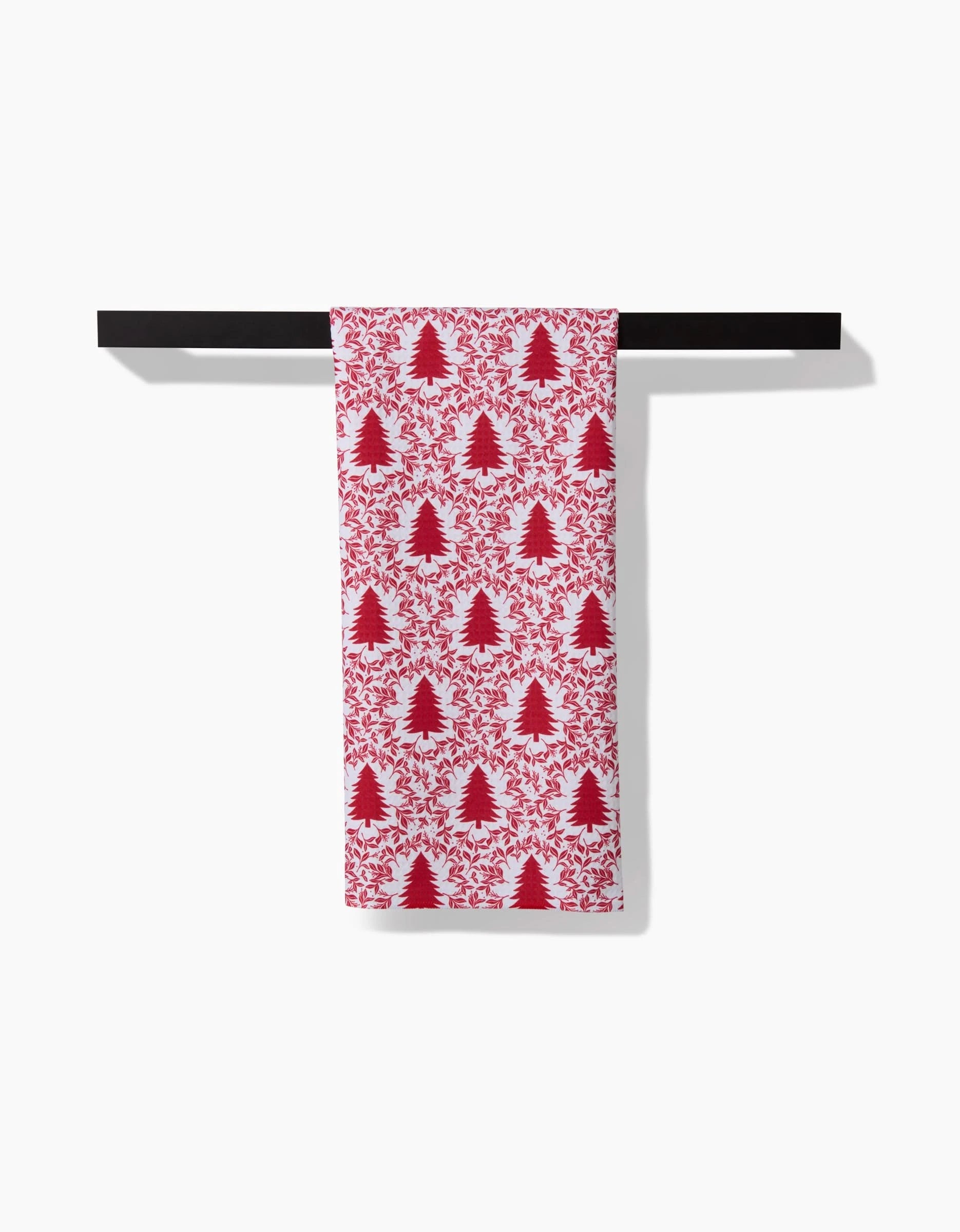 The Holiday Tree hand towel by Charlie Rowan Designs, featuring red Christmas trees and leaves, hangs over a black bar. Made with Geoweave technology, it offers a soft, quick-drying feel against a white background.