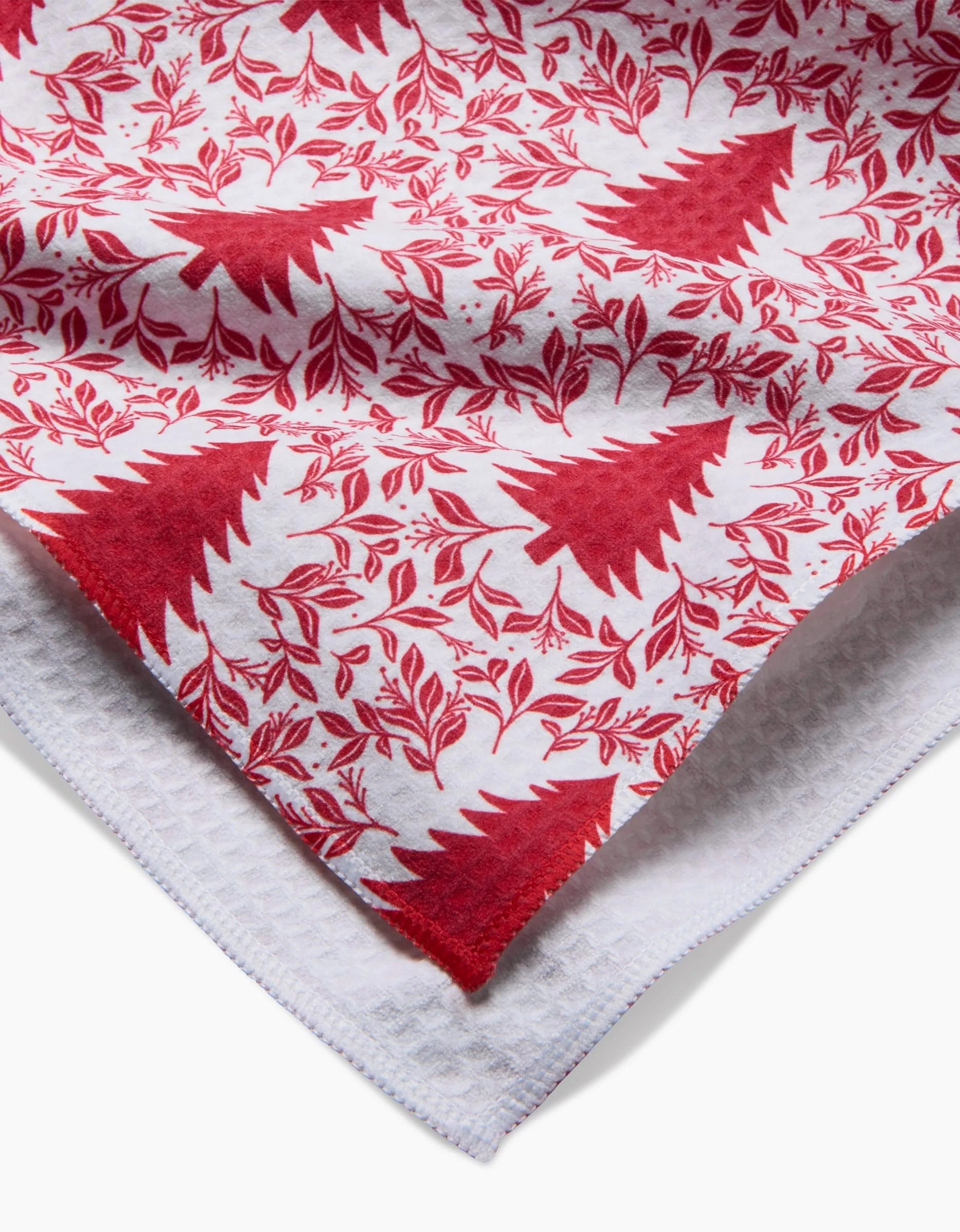 The Holiday Tree Luxe Hand Towel by Charlie Rowan Designs features red Christmas trees and foliage on white, layered over a textured cloth. Made with quick-drying Geoweave technology, its festive pattern brings holiday cheer.