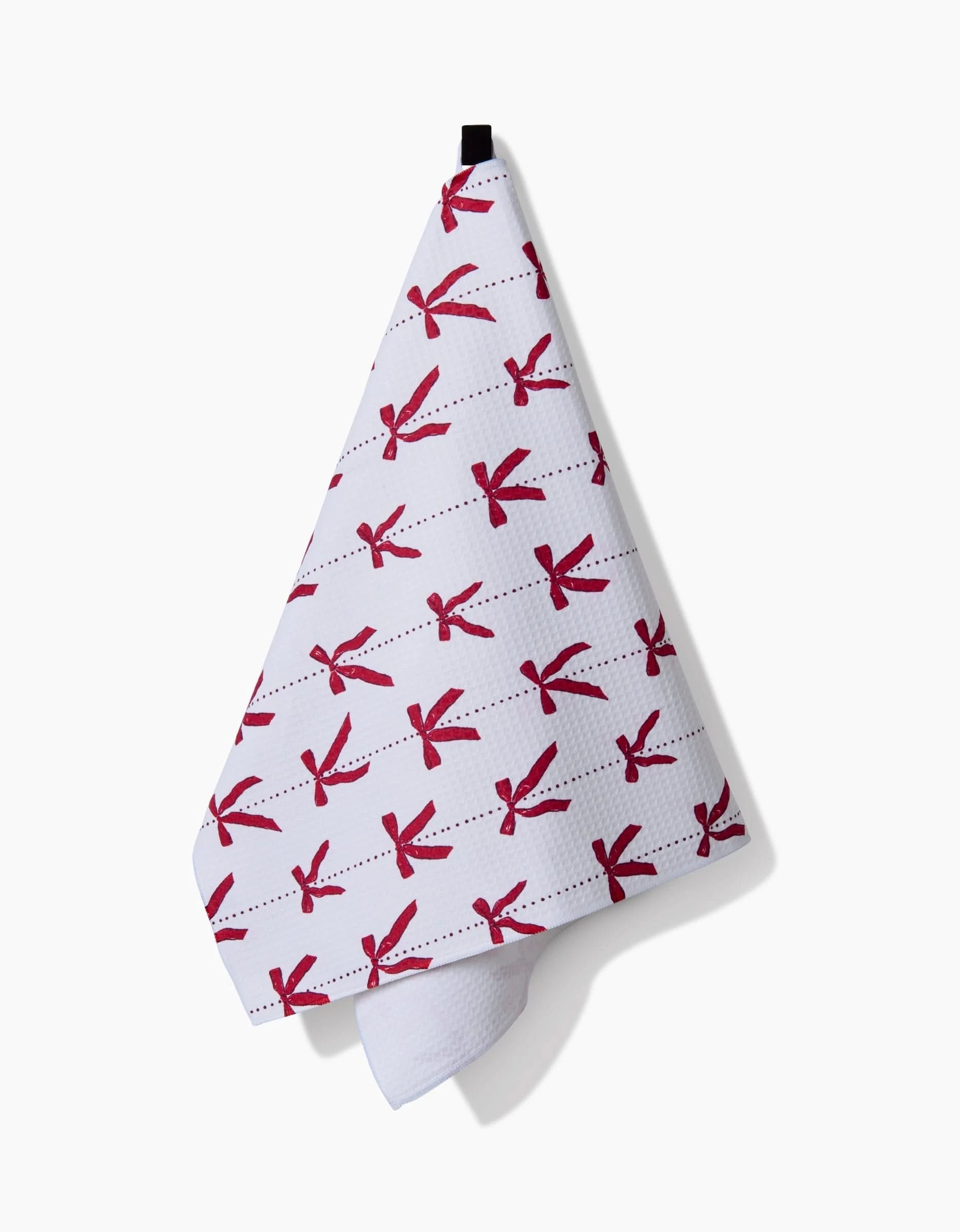 The Hufton Studio Little Bows And Pearls Luxe Hand Towel, featuring red bows on white and Geoweave technology for quick drying, hangs from a black loop against a white background with a soft shadow to the right.