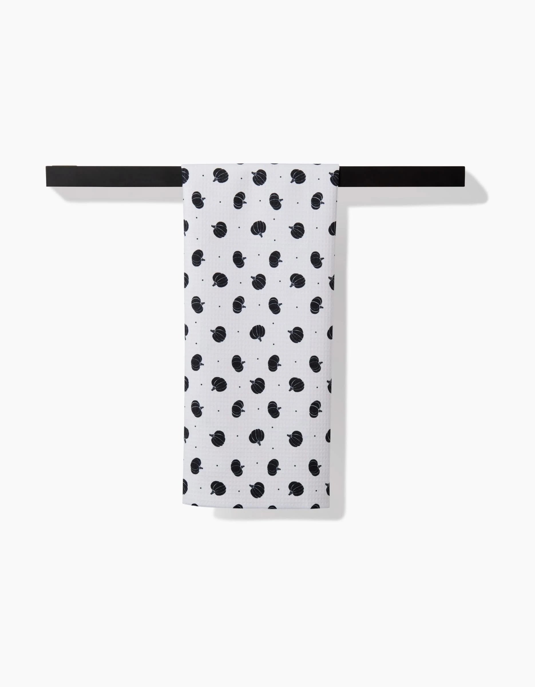The Ash Cascade Midnight Pumpkin hand towel, with its black dotted design, hangs over a horizontal black towel bar, providing ultra-absorbent comfort against a clean white background.