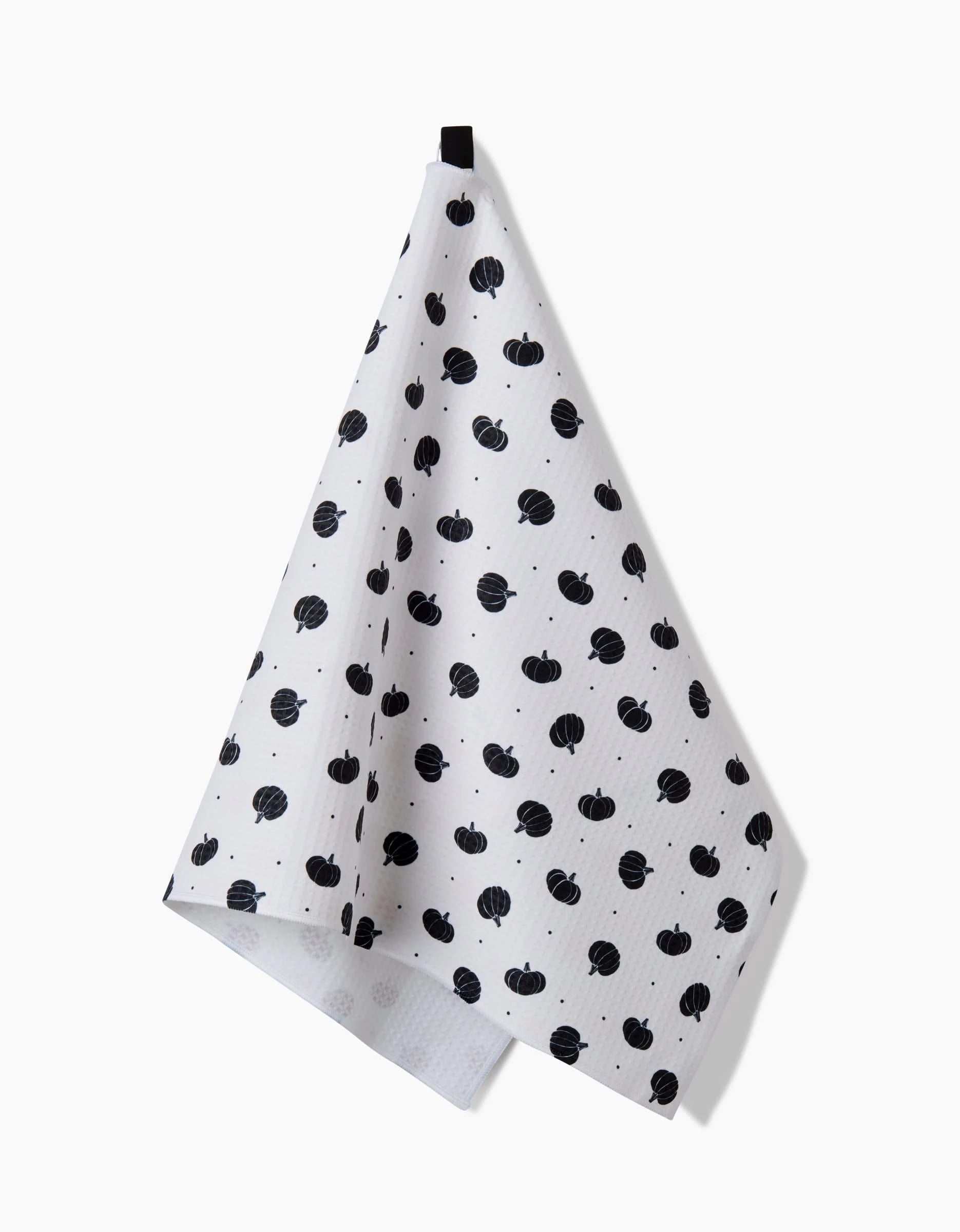 The Ash Cascade Midnight Pumpkin Luxe Hand Towel, featuring small black pumpkins on white, hangs from a black loop against a plain background—ultra-absorbent and the perfect stylish accent for any kitchen.