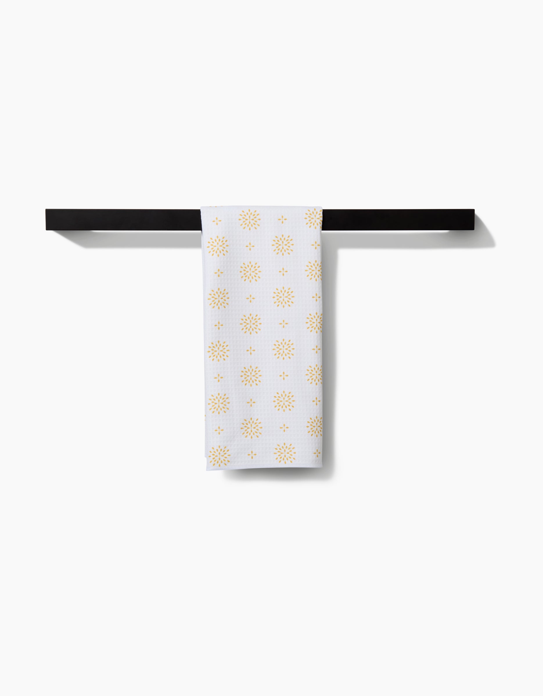 The Danelys Sidron Morning Petals Luxe Hand Towel, featuring ultra-absorbent Geoweave technology and small gold sunburst patterns, hangs neatly on a black rack against a plain white background.