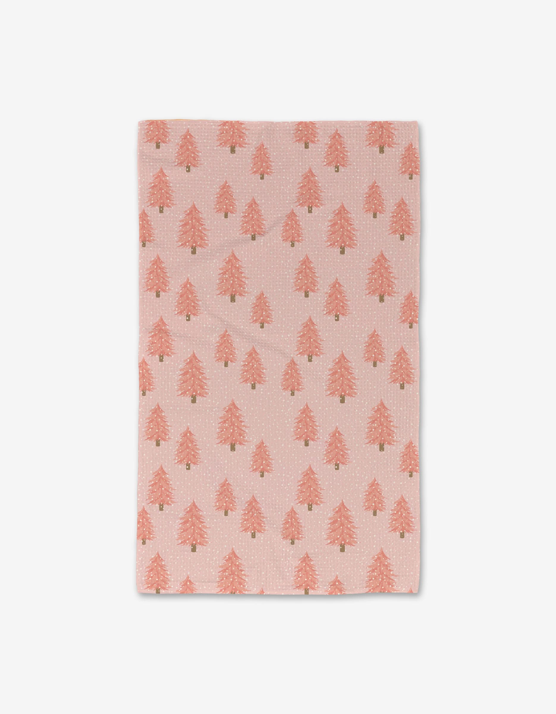 The Pink Christmas Luxe Hand Towel by Megan Kampa is a light pink rectangular towel with a pattern of small, red Christmas trees evenly spaced on an ultra-absorbent white background.