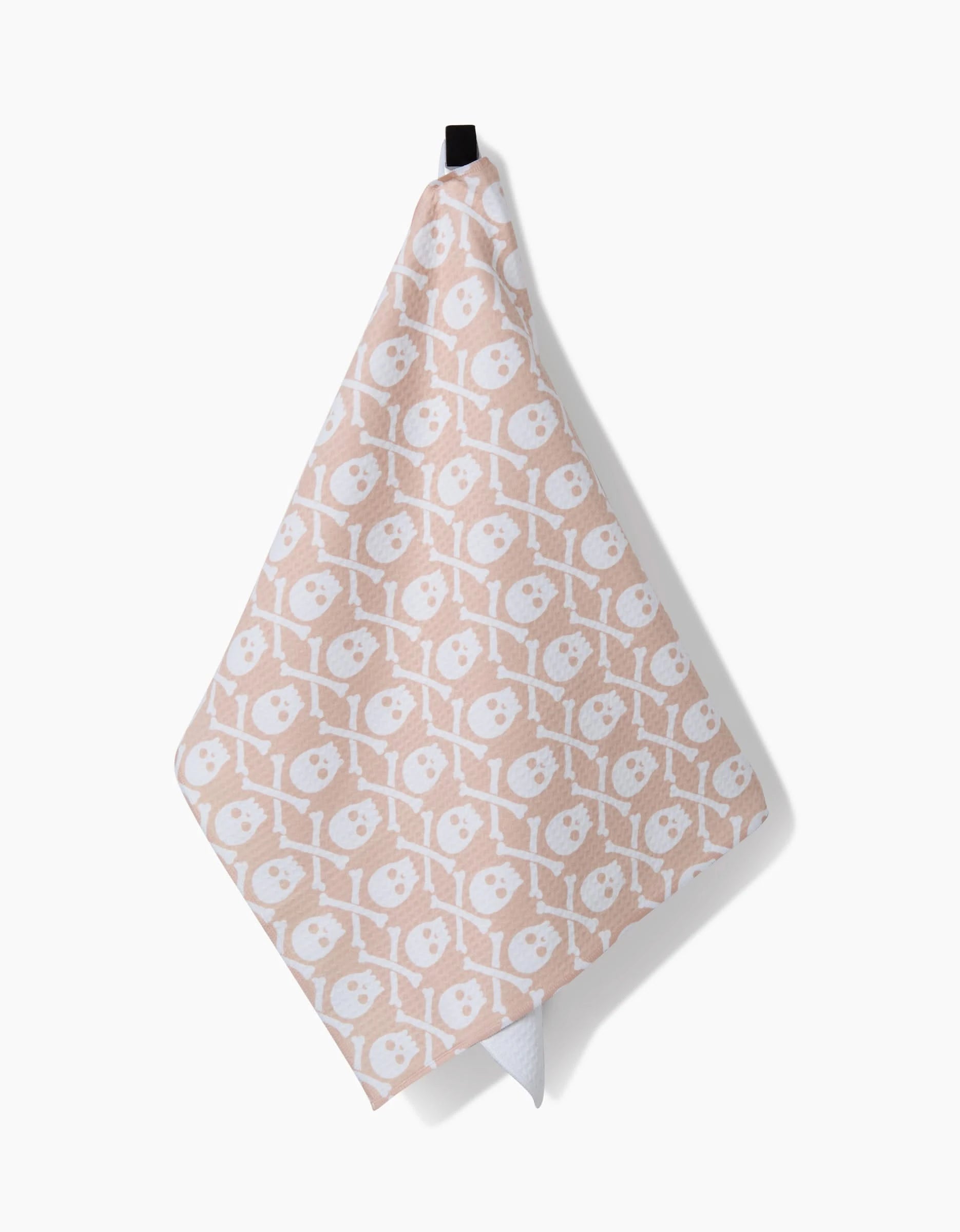 The Hufton Studio Skull Bones Natural hand towel, beige with a white repeating skull and crossed bones pattern, ultra-absorbent and quick-drying, hangs by a black loop against a plain white background.