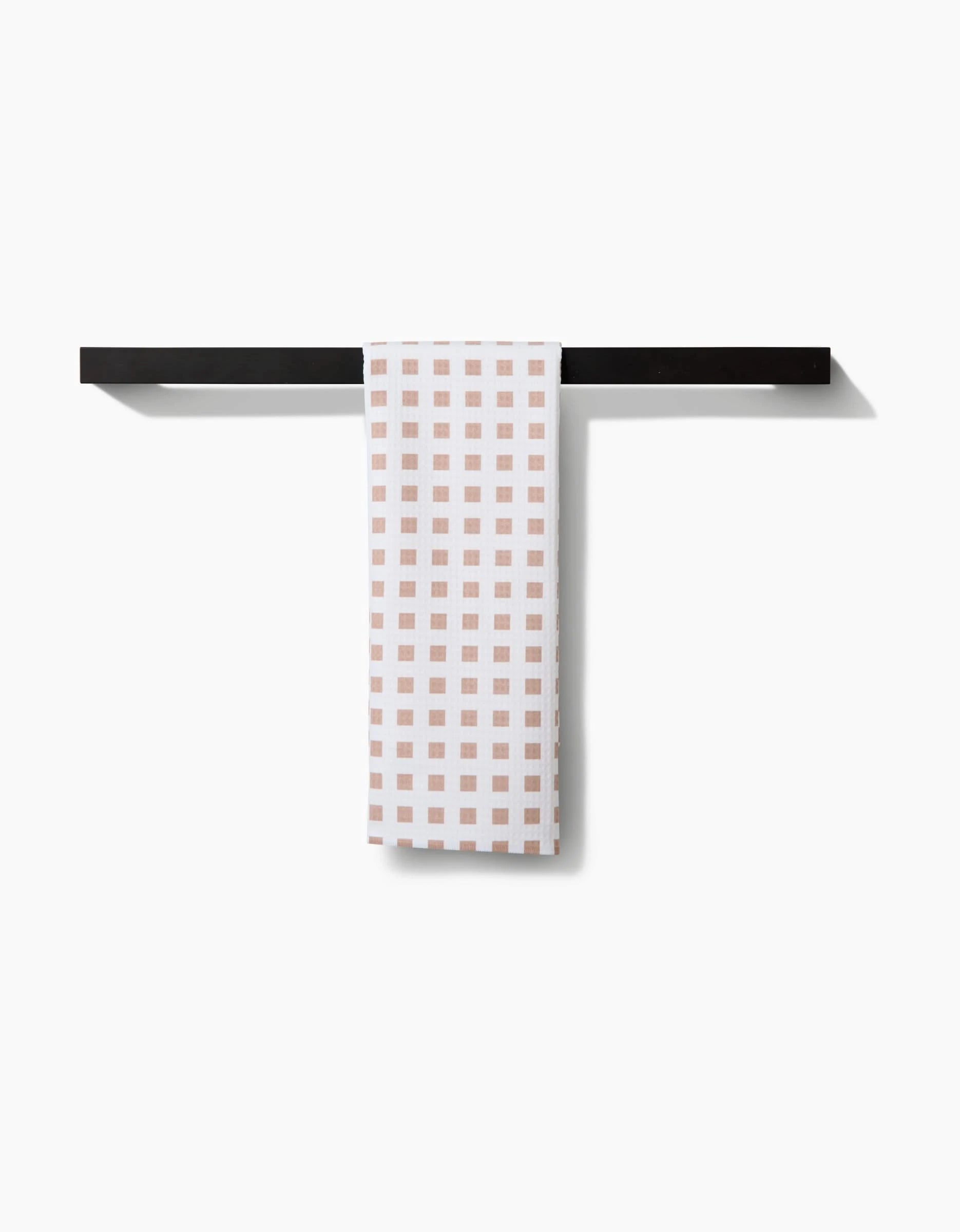 The GEOMETRY Spring Square towel, featuring a beige checkered design and ultra-absorbent Geoweave technology, hangs neatly on a straight black bar against a plain white background.