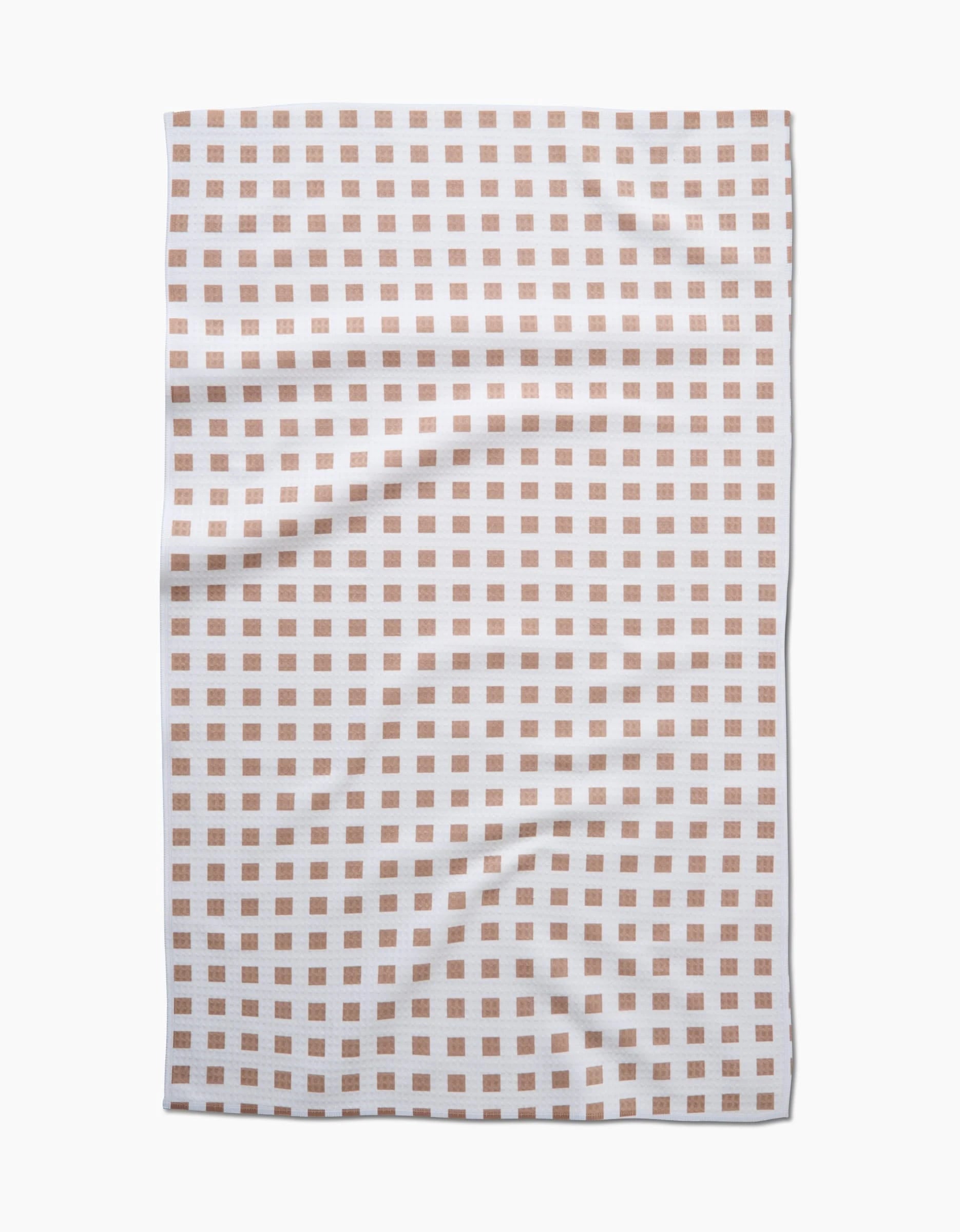 The GEOMETRY Spring Square towel features evenly spaced light brown squares on white, photographed from above with a slightly wrinkled look. Made with quick-drying Geoweave technology for both convenience and style.