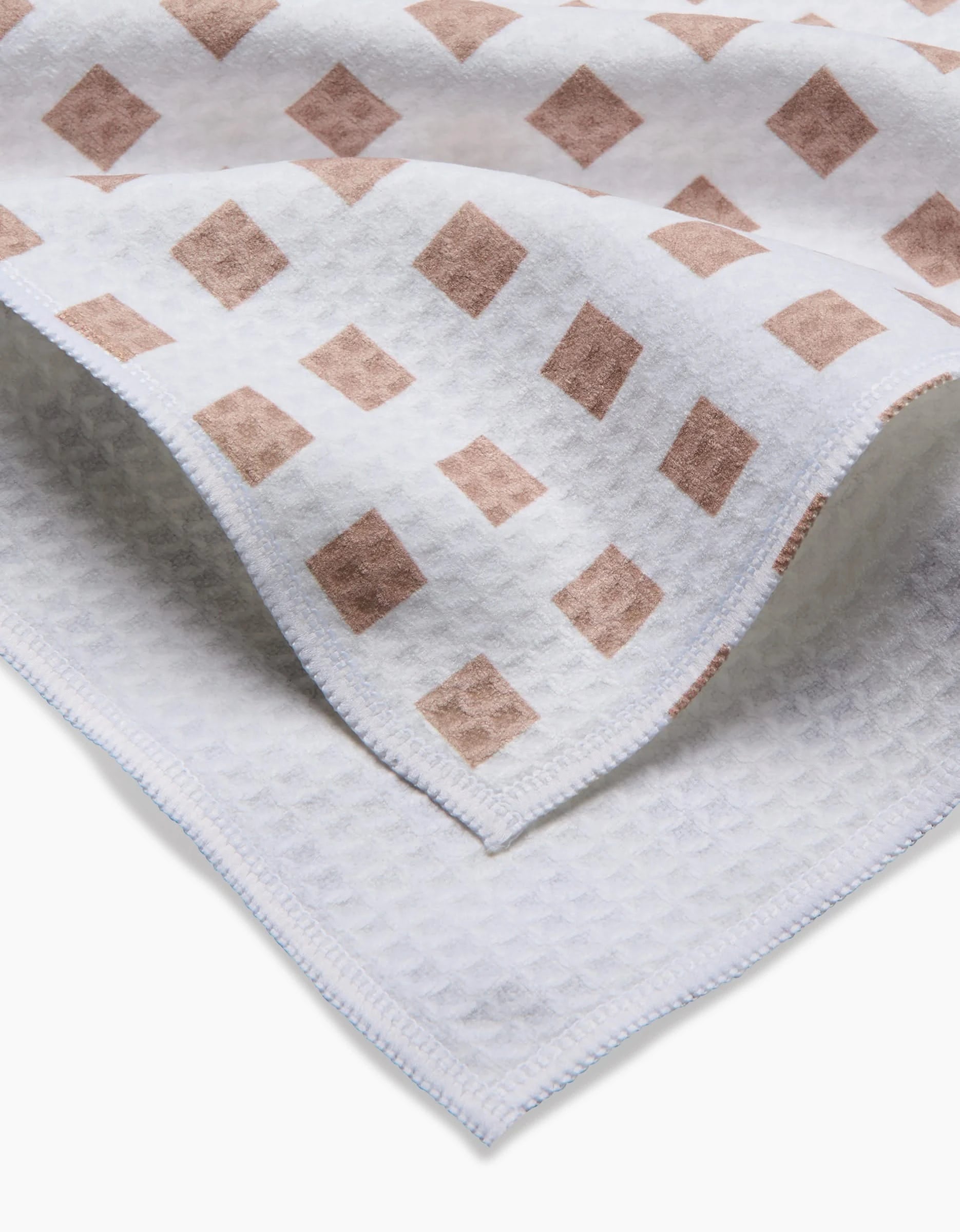 A close-up of the GEOMETRY Spring Square towel, featuring a white ultra-absorbent waffle texture, neatly stitched edges, and a corner adorned with light brown diamond shapes. This towel is designed for quick drying.