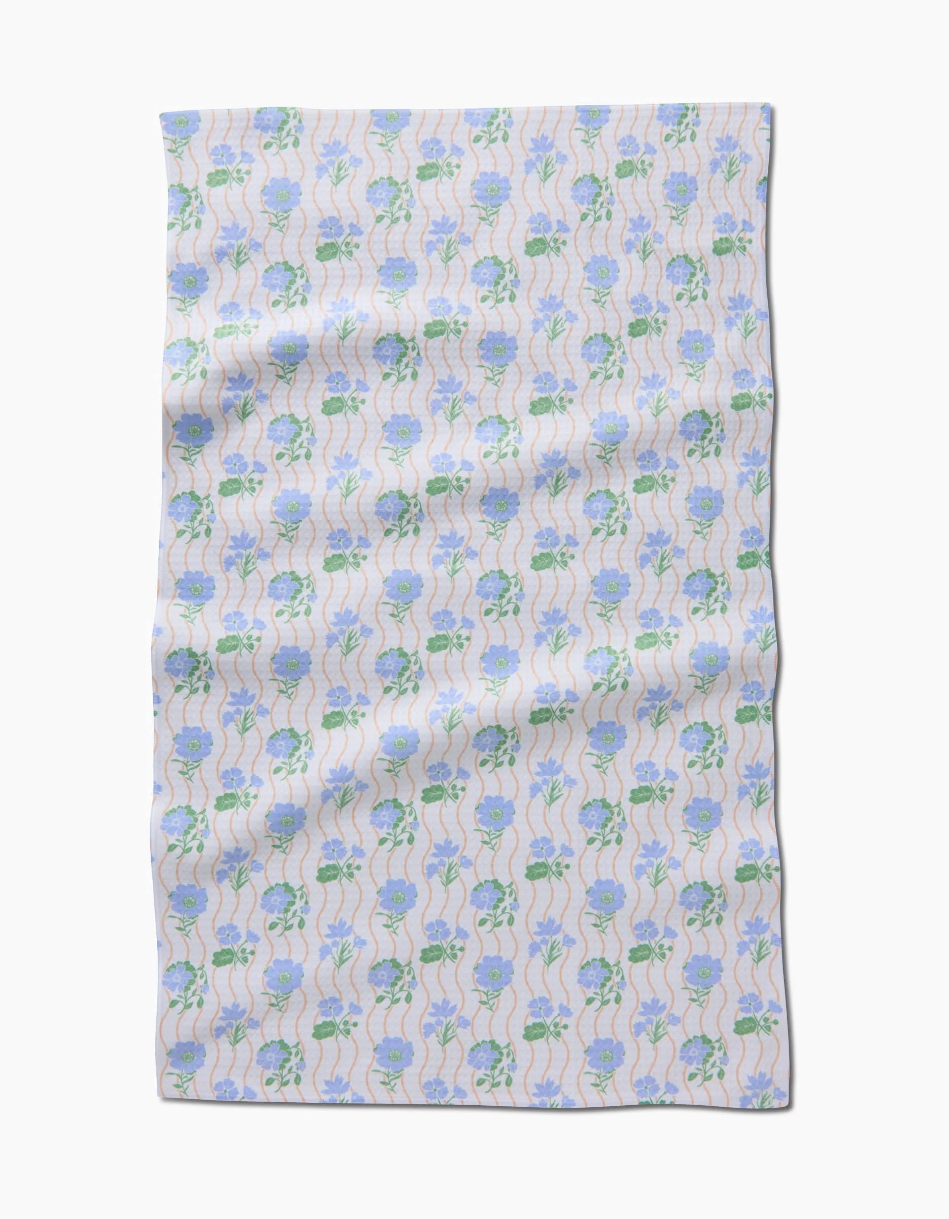 The Spring Wave by Danelys Sidron is a rectangular cloth showcasing light blue flowers with green stems on white, displayed flat with gentle wrinkles. Crafted with ultra-absorbent, quick-drying Geoweave technology.