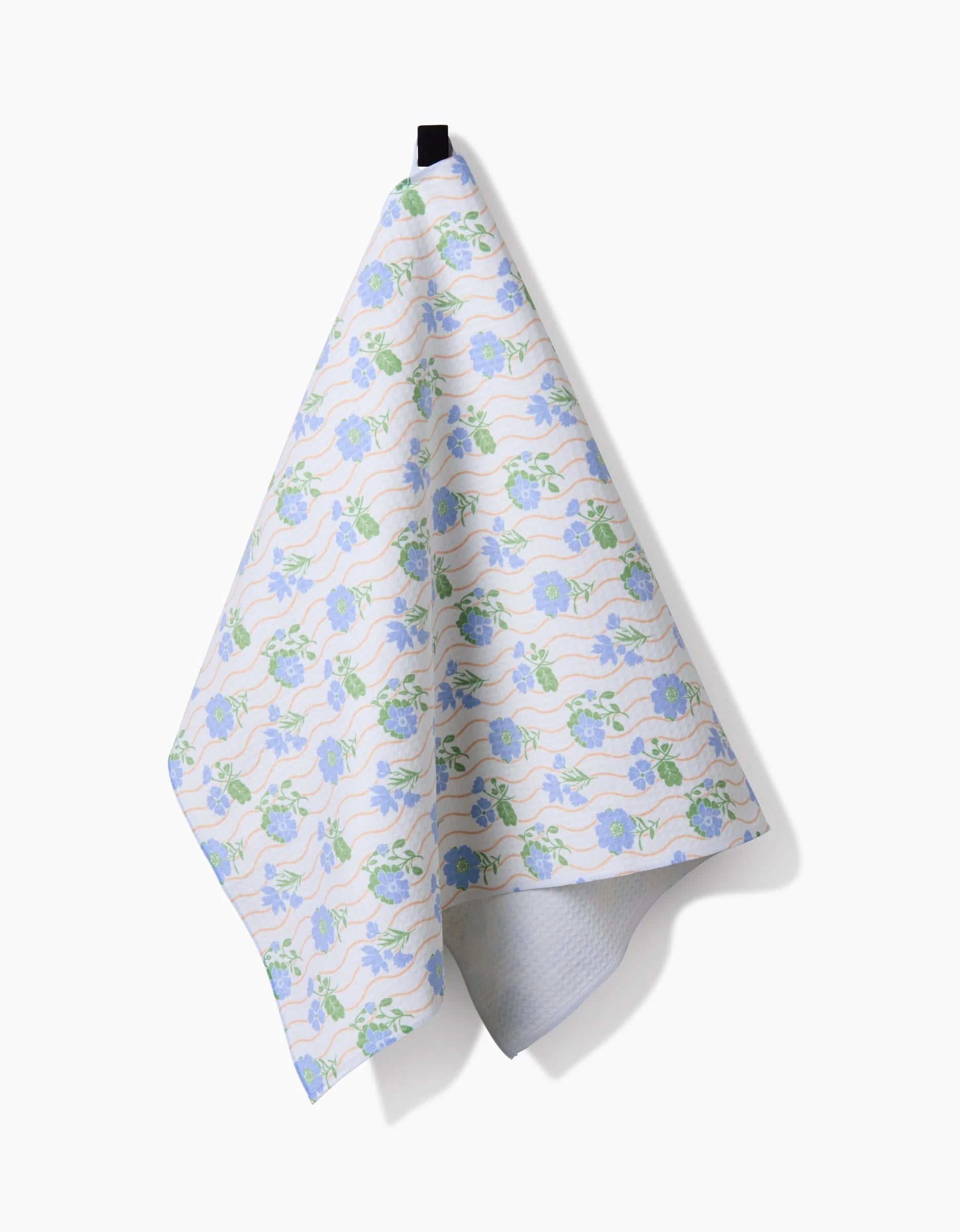 The Danelys Sidron Spring Wave dish towel, featuring blue and green florals and made with ultra-absorbent Geoweave technology, hangs from a black hook against a plain white background.