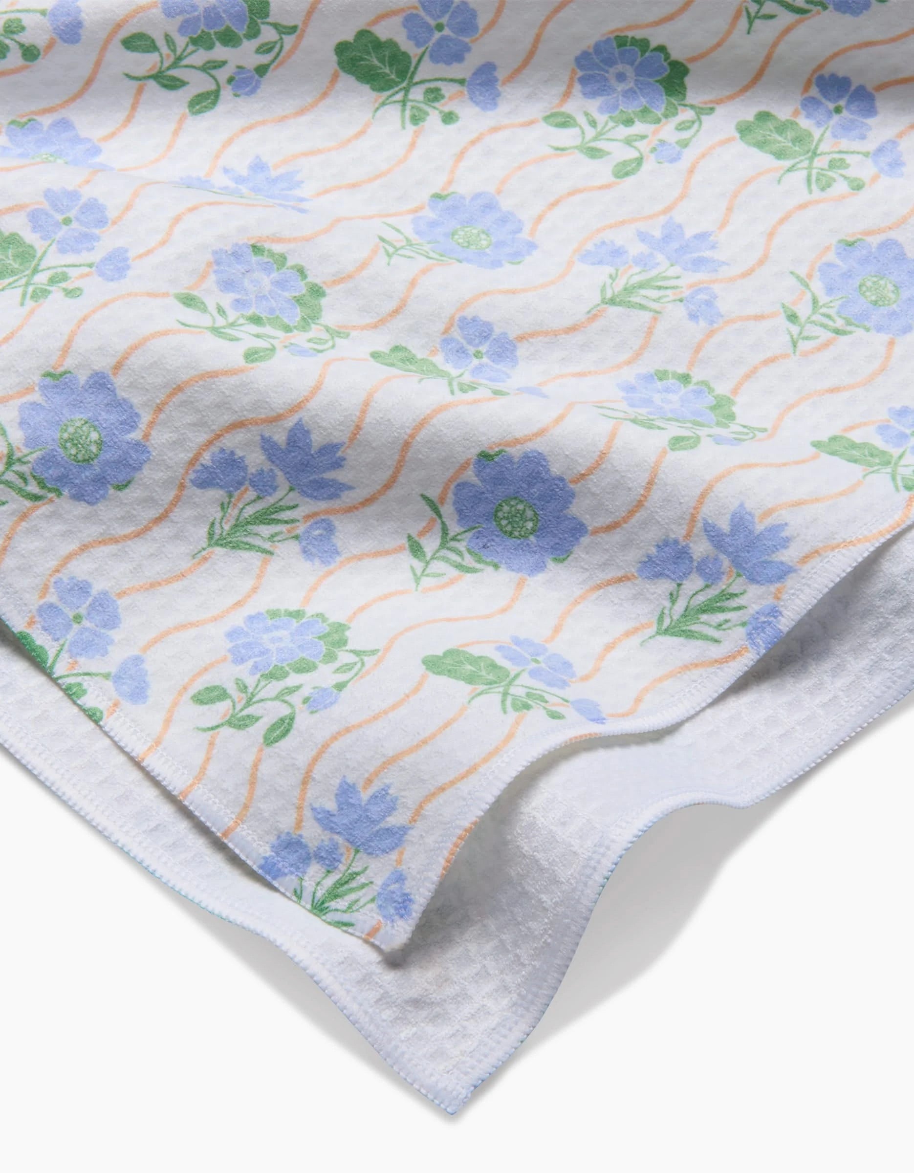 Spring Wave by Danelys Sidron—a white fabric with blue and green floral patterns and orange wavy lines, featuring quick-drying Geoweave technology—draped over a textured white surface.