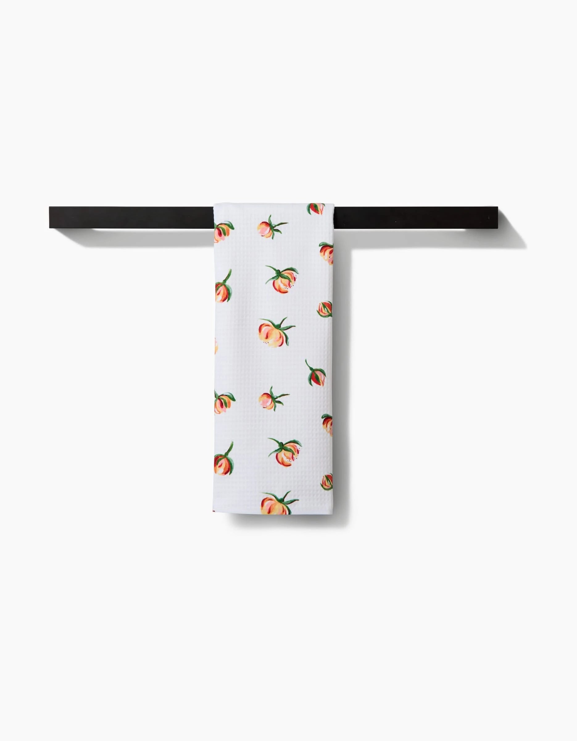 A white, ultra-absorbent kitchen towel with a yellow rosebud pattern by Linda Fox hangs neatly over a simple black towel bar against a white background.