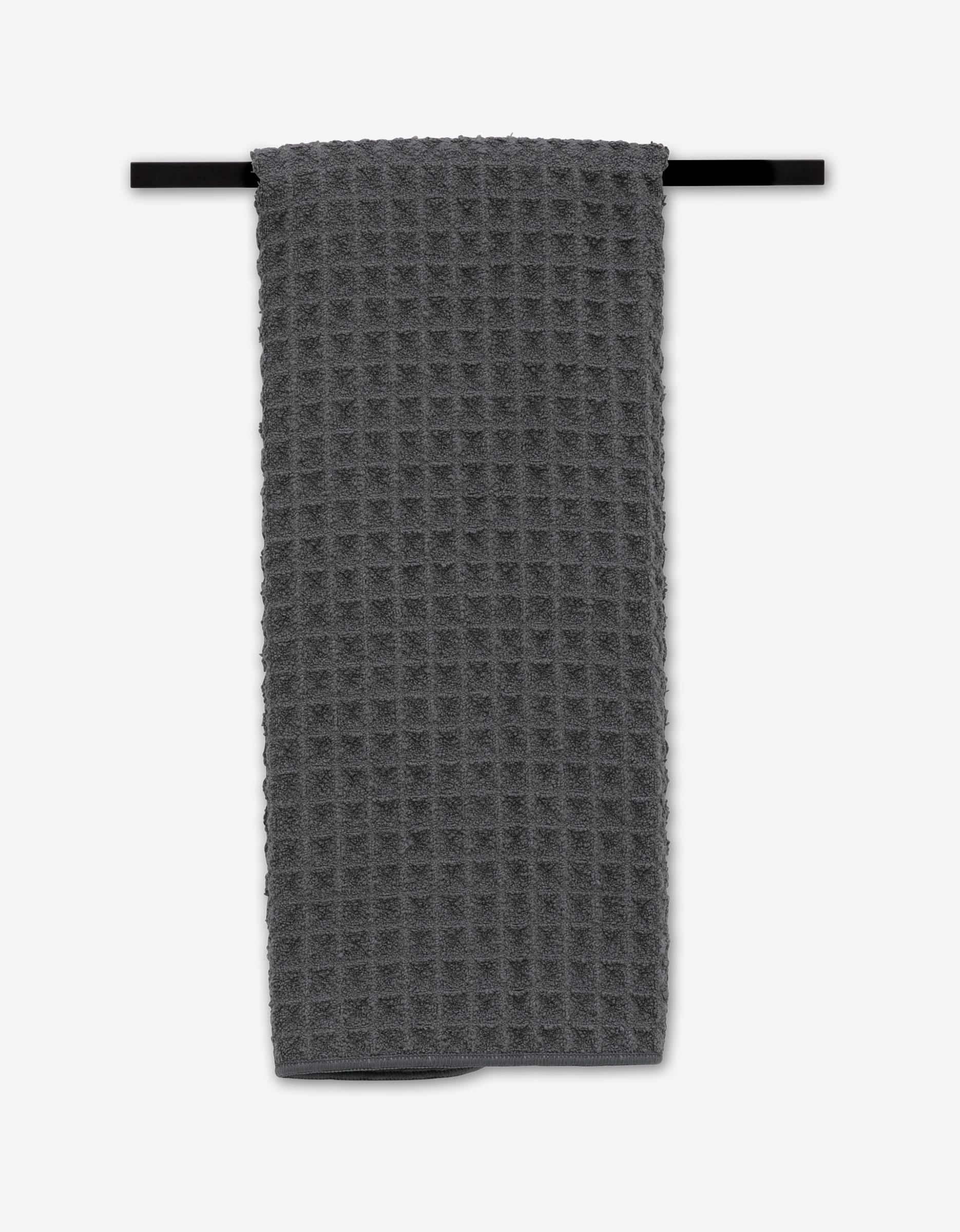 The GEOMETRY Charcoal Hand Towel with a dark gray waffle pattern hangs neatly folded over a horizontal black towel bar against a plain white background.