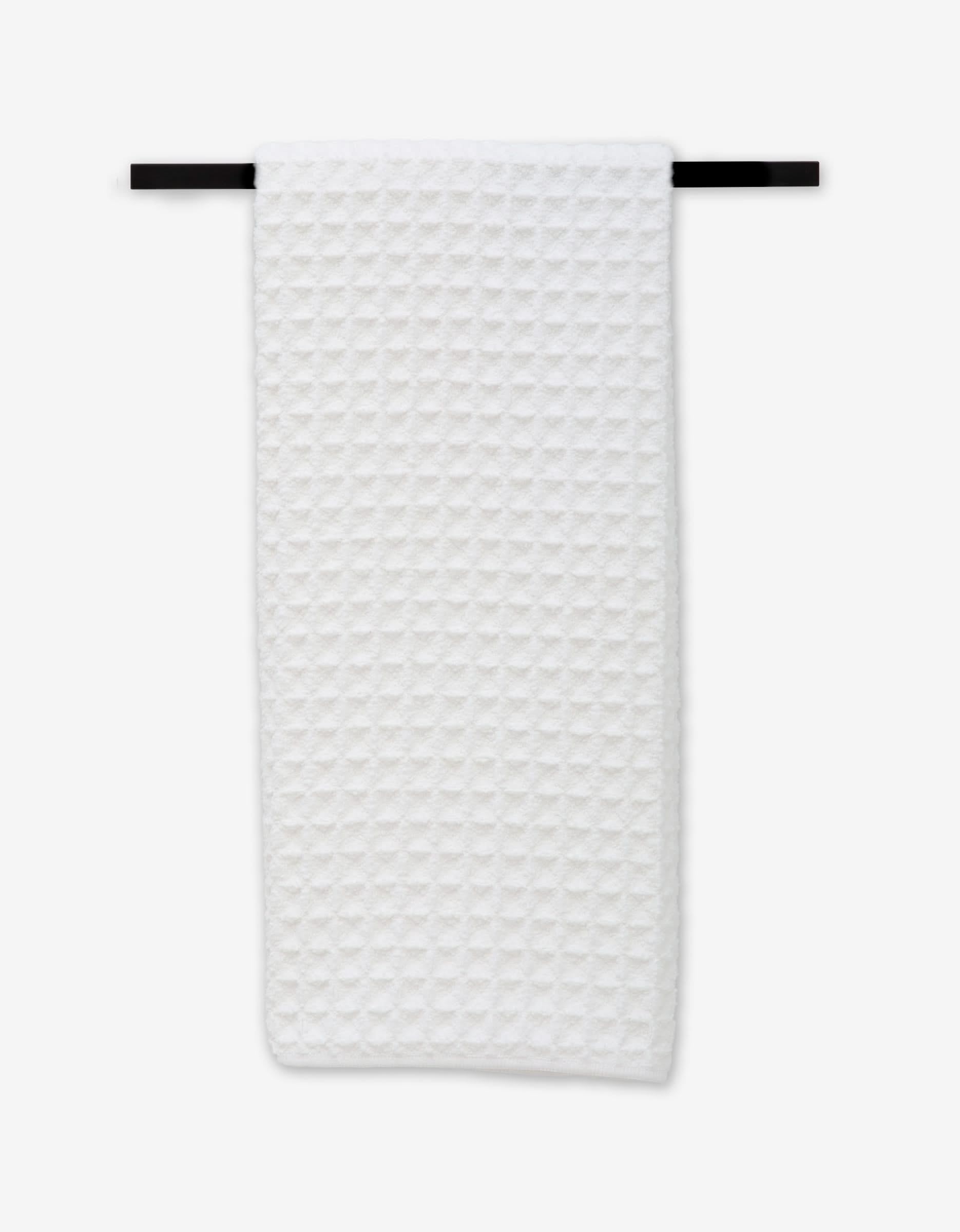 The GEOMETRY Cloud hand towel, featuring a white textured waffle design, is neatly draped on a black towel bar against a plain background, adding subtle elegance to any space.