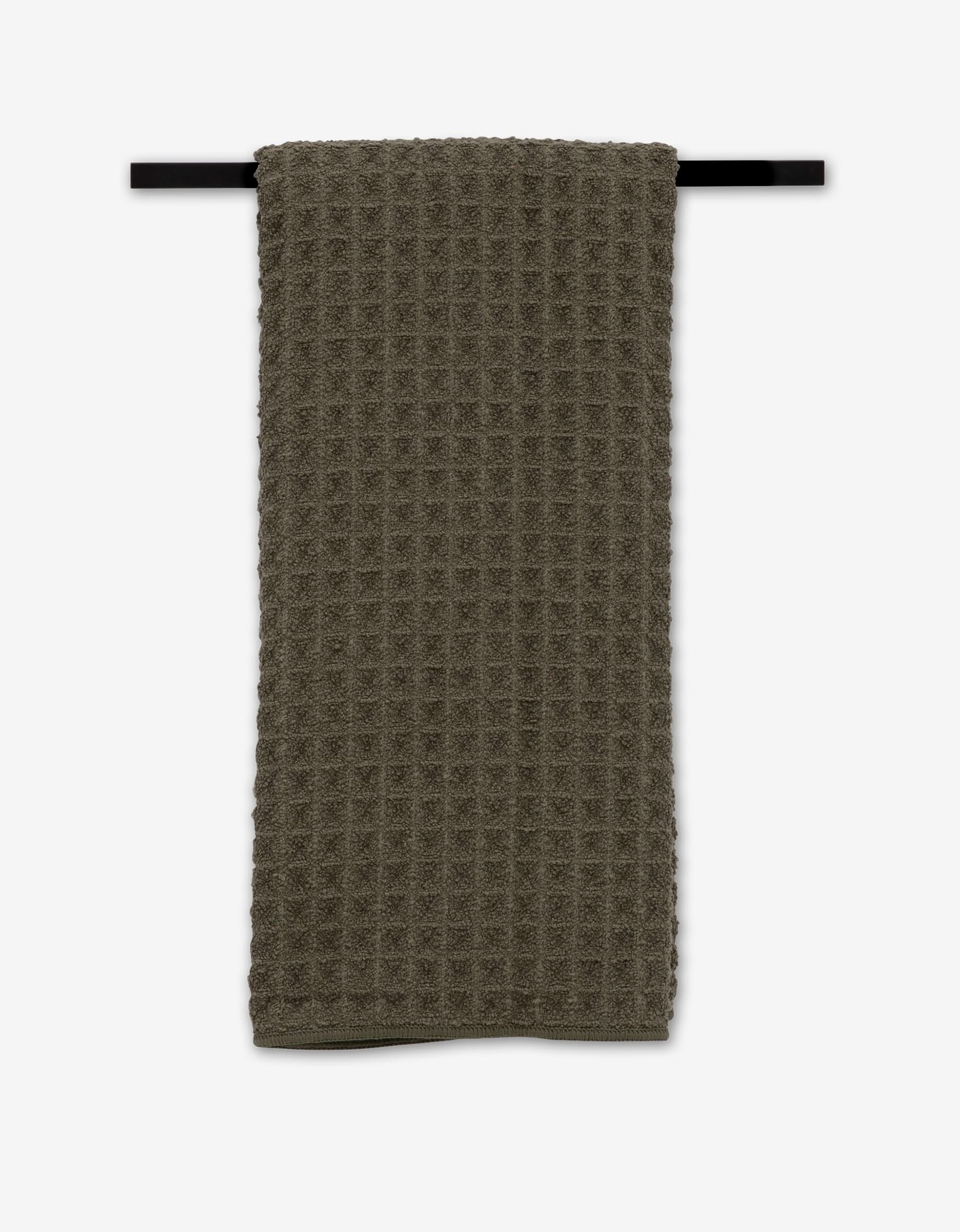The GEOMETRY Forest towel, in dark green with a waffle texture, hangs neatly on a black bar against a white background.