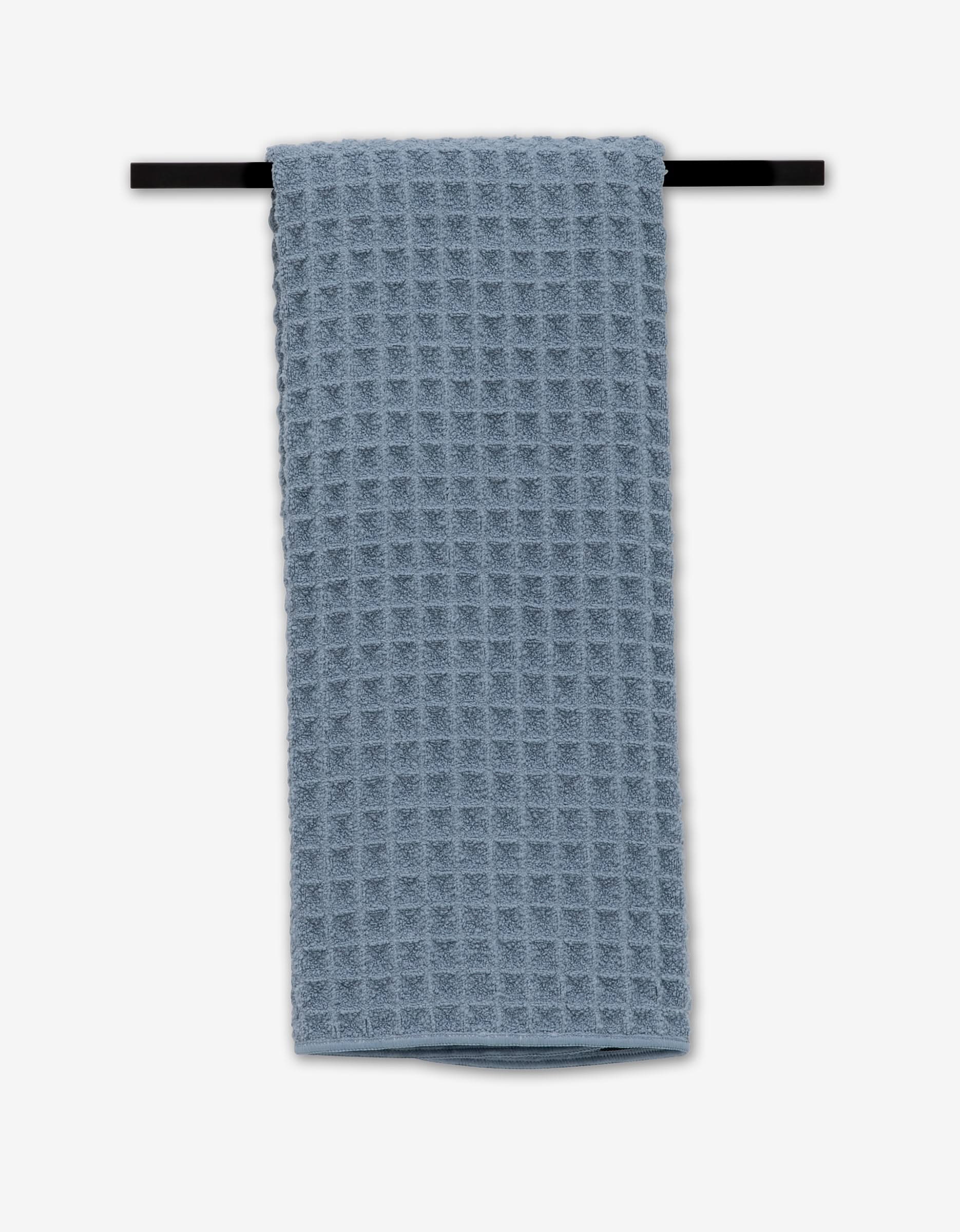 The GEOMETRY Sky hand towel, ultra-absorbent and luxuriously soft, hangs neatly on a black towel bar against a plain white background.