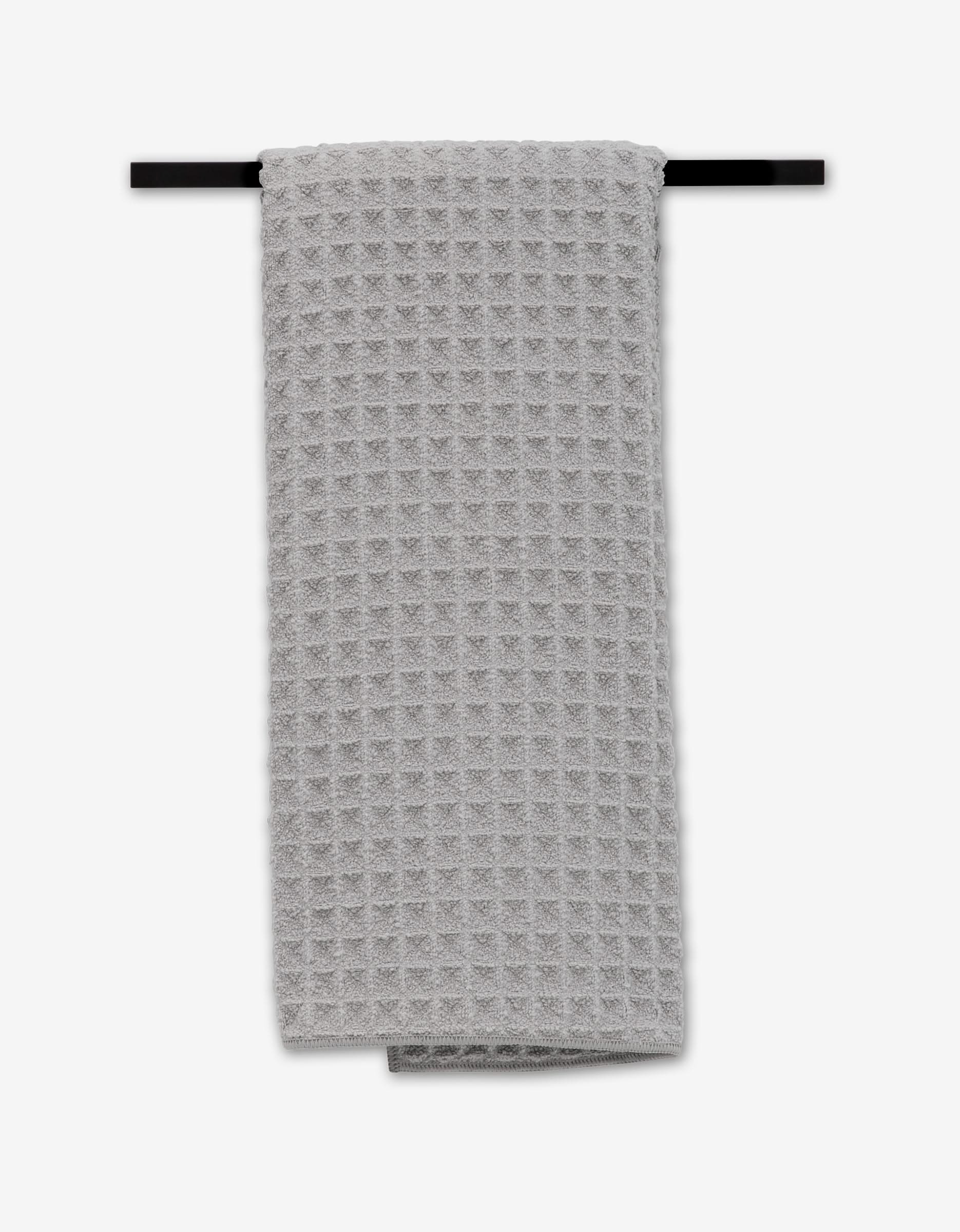 The GEOMETRY Stone Hand Towel, featuring a luxurious light gray waffle weave pattern, is neatly folded on a black towel bar against a white background. Ultra-absorbent and stylish, it brings elegant simplicity to any bathroom.