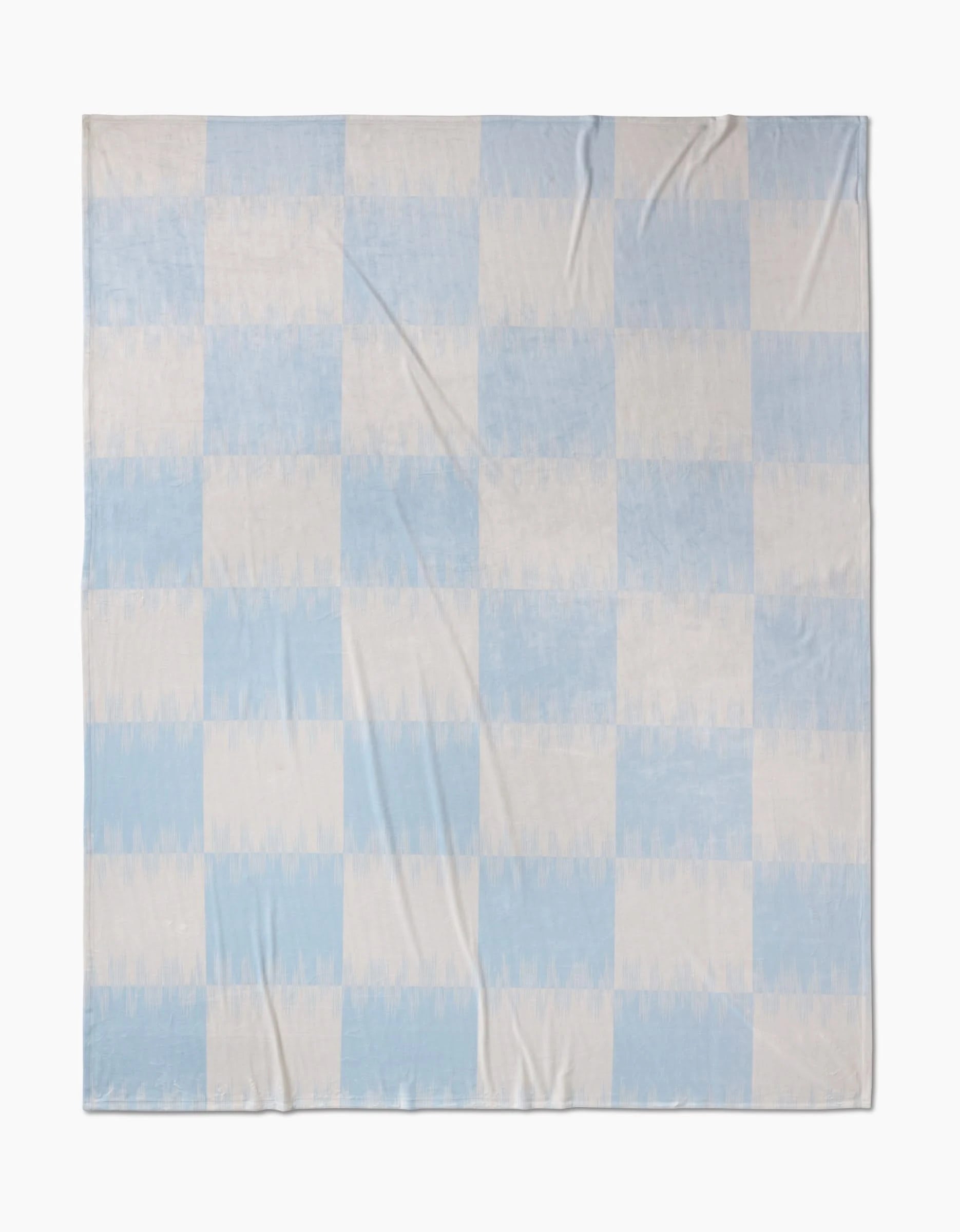 The Geometry Sweet Checks Butter Blanket showcases a simple checkered pattern with light blue and off-white squares, crafted from recycled materials. It’s laid flat, highlighting its soft fabric folds.