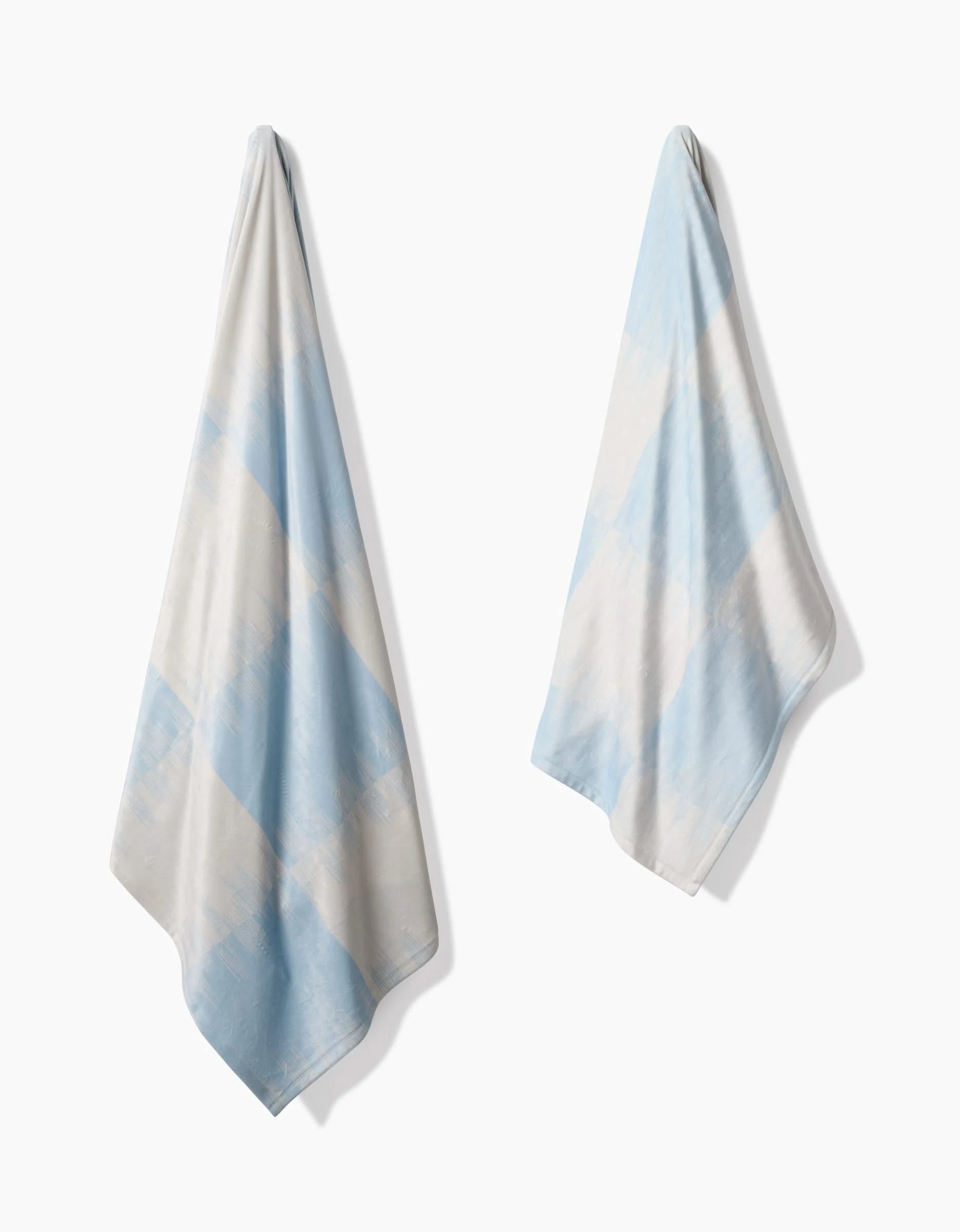 Two light blue and white Geometry Sweet Checks towels, made from recycled materials, feature a soft diagonal checkered pattern and hang separately against a white background.