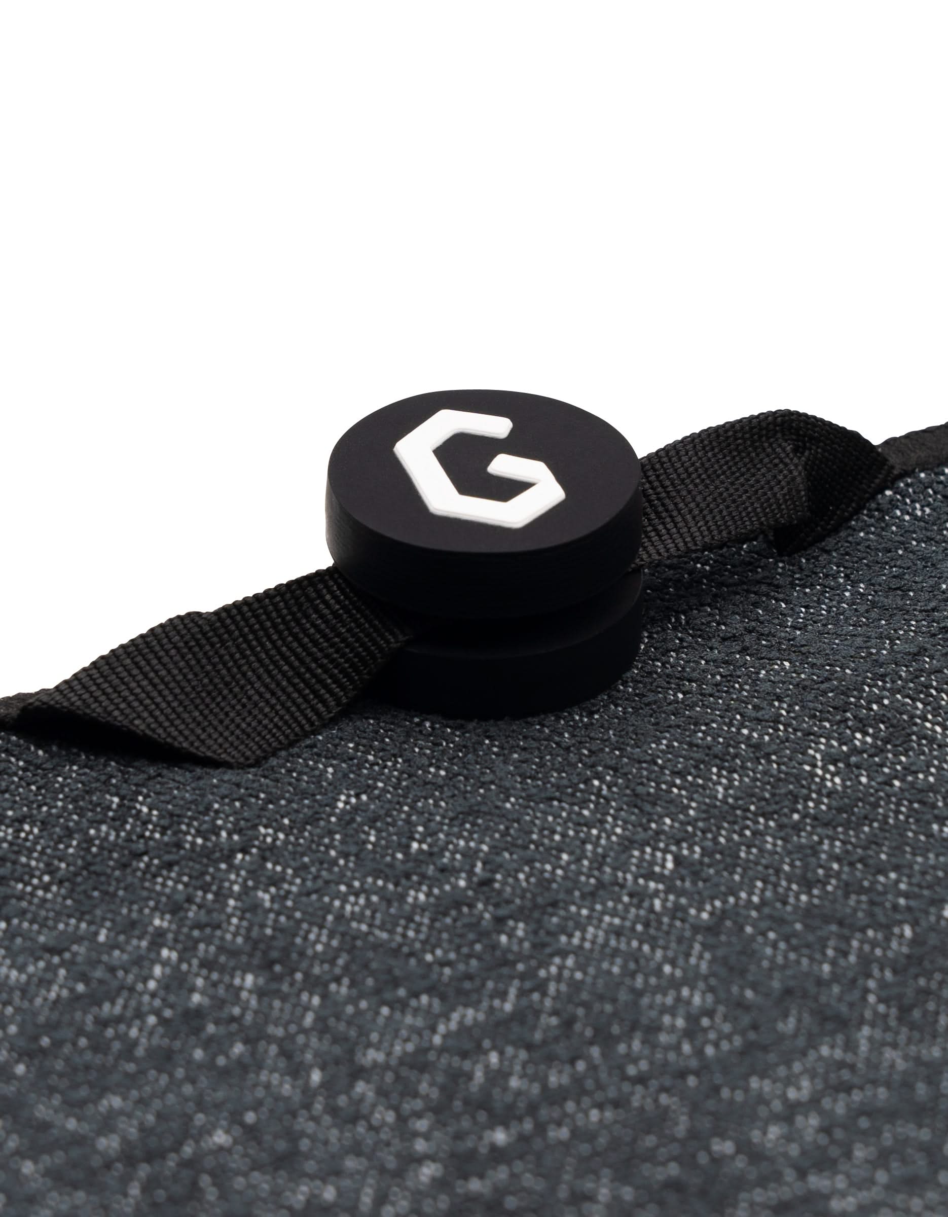Black circular object with a white “G” logo attached to a textured dark gray GEOMETRY gym towel, Magna - The Soul, using a black fabric loop—perfect for keeping your towel handy during workouts.