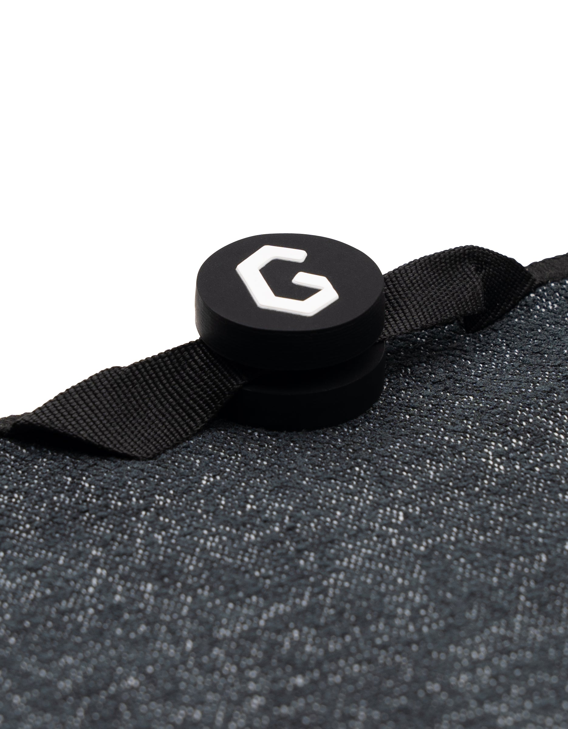 A close-up of the Magna - Bohemian Mosaic fitness towel by GEOMETRY, featuring a textured black recycled material and a round black clip with a white G logo attached by a black strap.