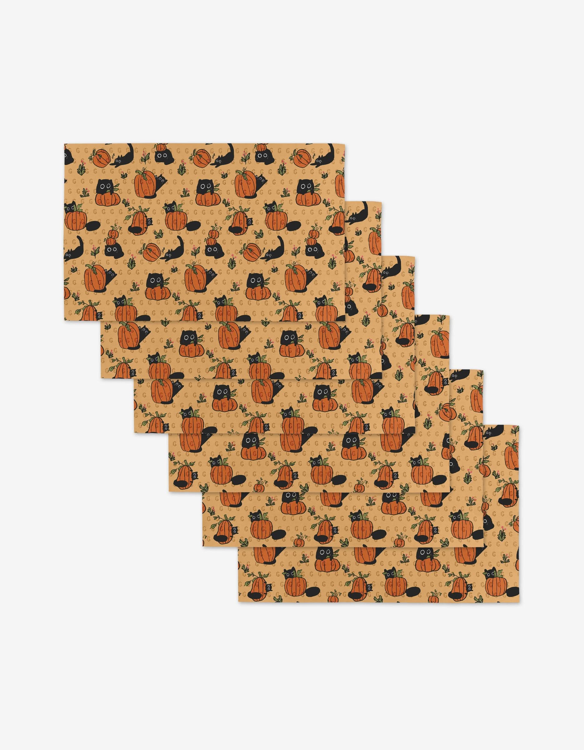 Six Janna Sue Design Black Cats placemats with Halloween motifs—black cats, pumpkins, witch hats, and leaves on tan—are stacked in a fanned display. Eco-friendly materials used.