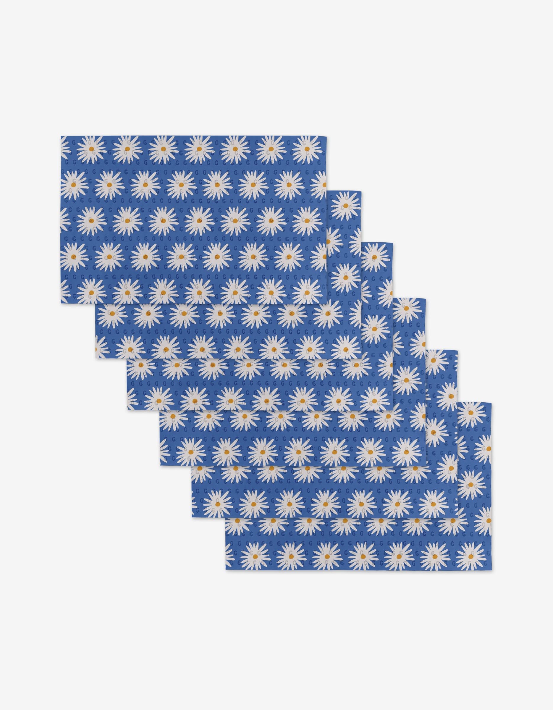 Six Blue Daisies rectangular placemats by Megan Roy, featuring a repeating white daisy pattern on blue, are arranged in an overlapping stack—a reusable, eco-friendly alternative to Not Paper Towels for your table.
