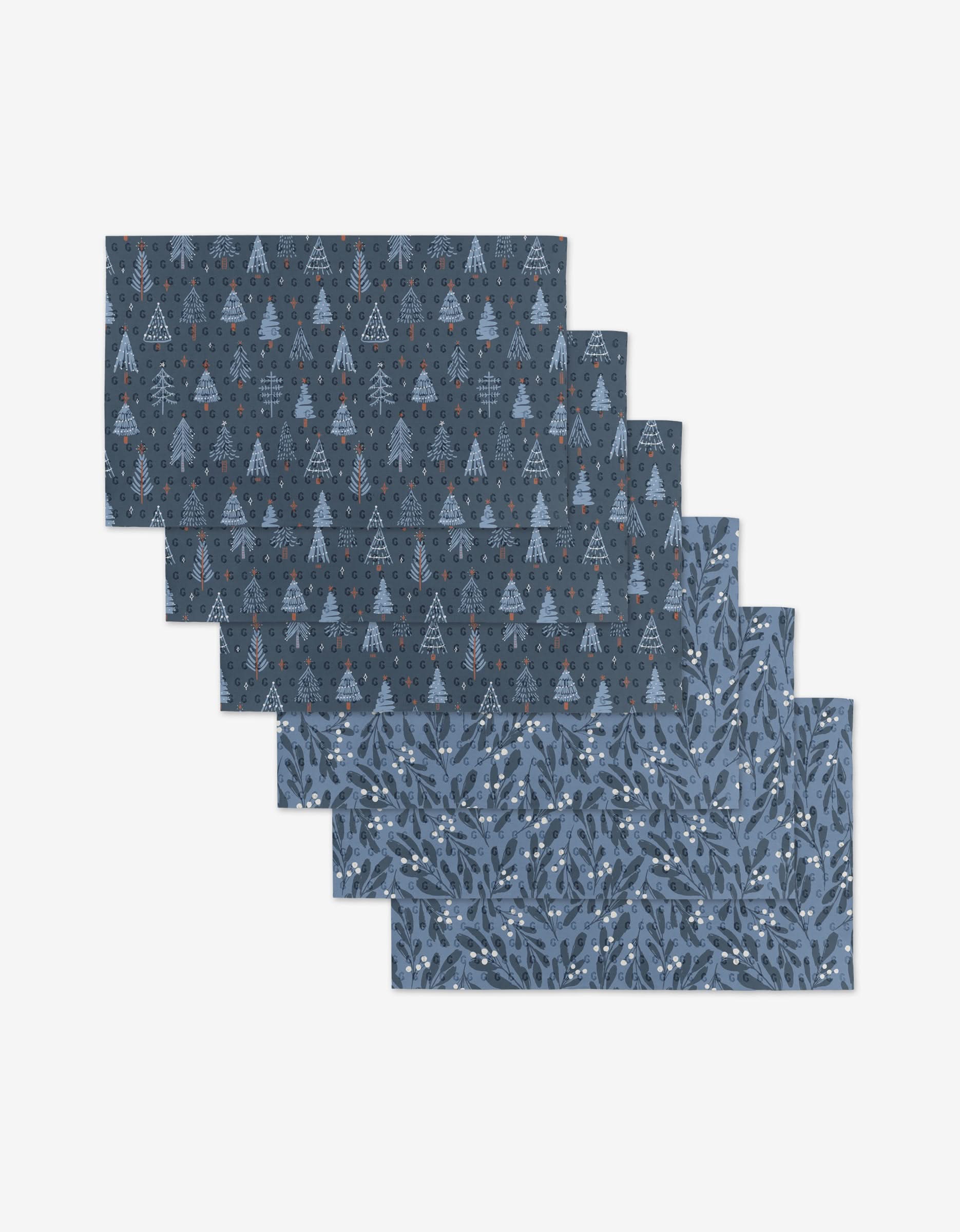 Six reusable Blue X-Mas cloth napkins by Hufton Studio, arranged in a staggered stack: three with a dark blue geometric tree pattern, three with a blue leafy branch and berry design—a stylish, eco-friendly alternative to paper towels.