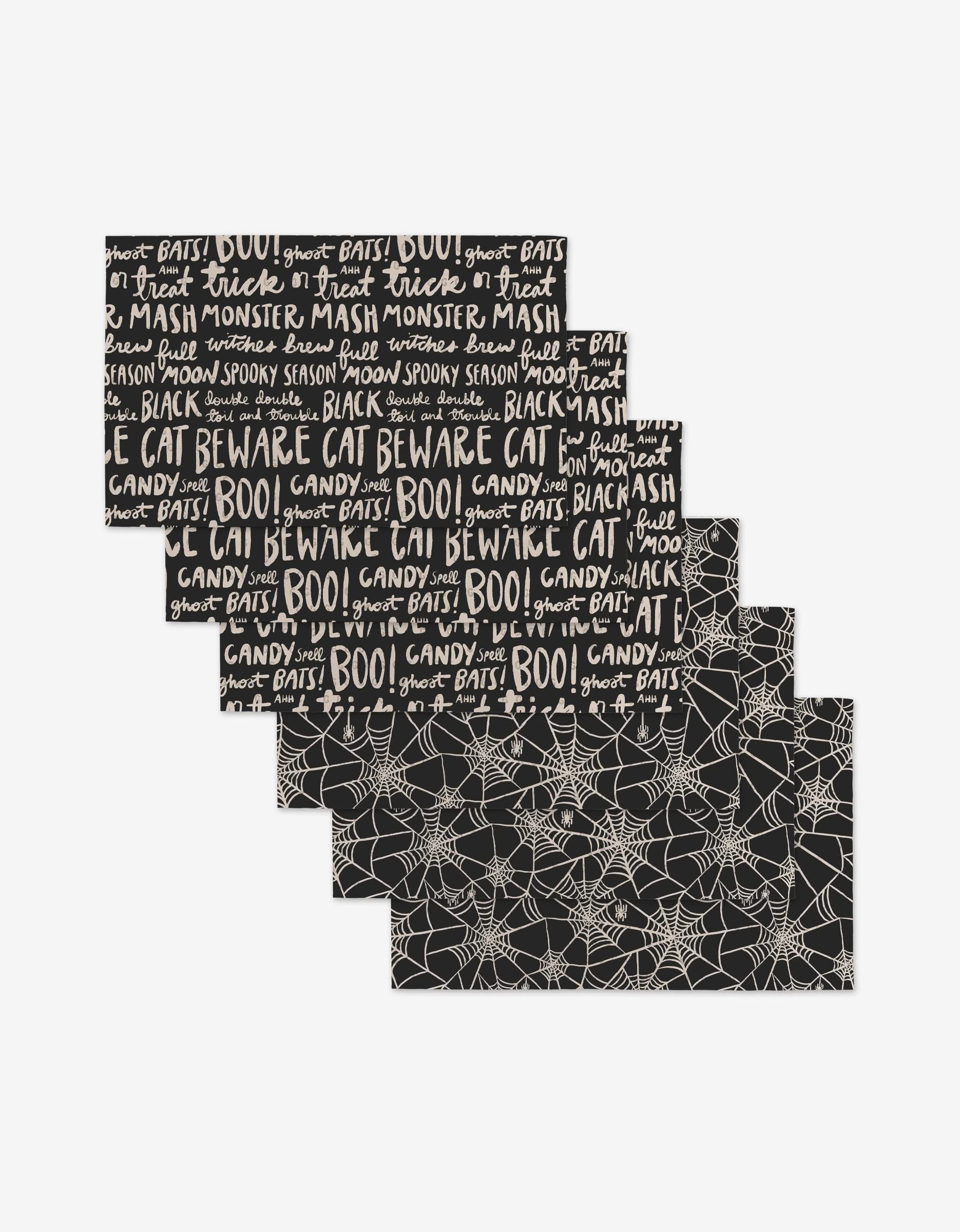 Five Kayla Ann Booos placemats are shown: three with Halloween words like BOO and Beware Cat on black, two with a white spiderweb pattern. These eco-friendly placemats are a great alternative to Not Paper Towels.