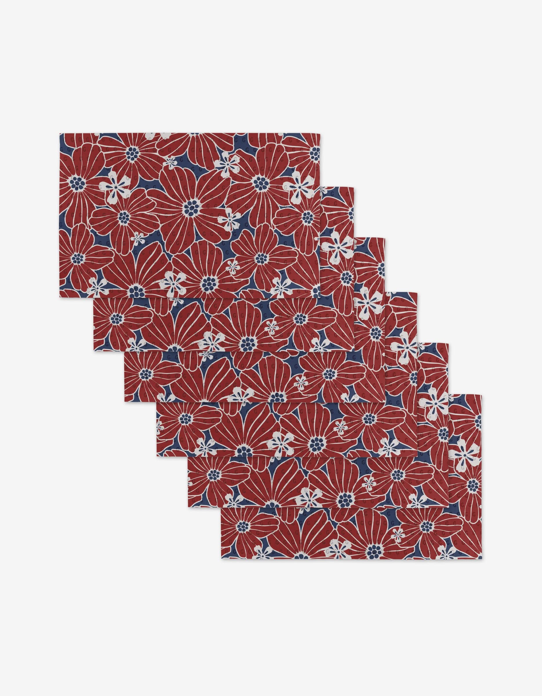 Six Botanical Blush rectangular placemats by Ashley Celena, featuring a red, white, and navy blue floral pattern with large flowers and leaves, are stacked in an overlapping arrangement against a white background. Made from eco-friendly materials.