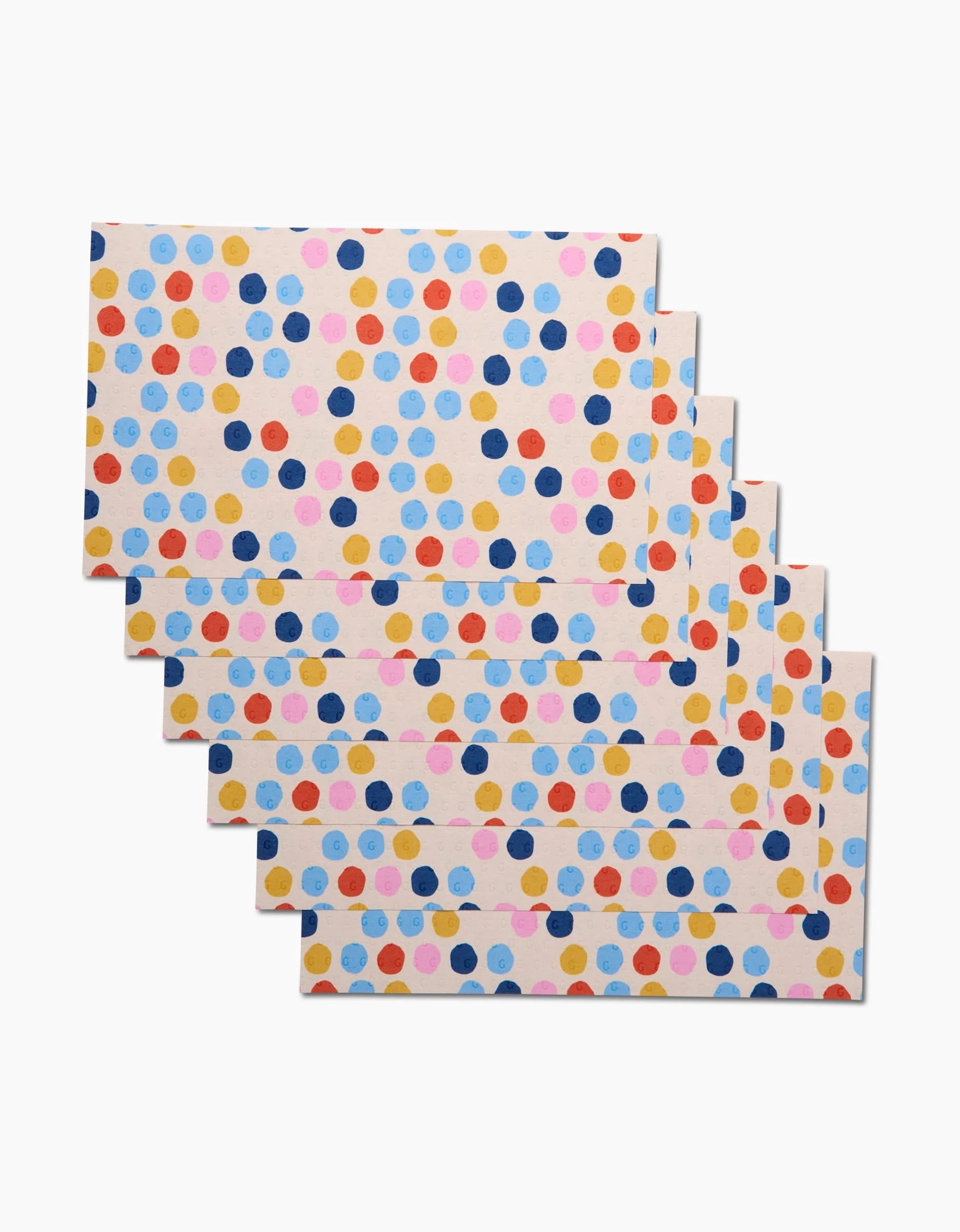 Six reusable Lizzie Clark Carnival placemats, featuring a vibrant polka dot design in blue, pink, yellow, and orange on a light background, offer an eco-friendly way to brighten up your table.