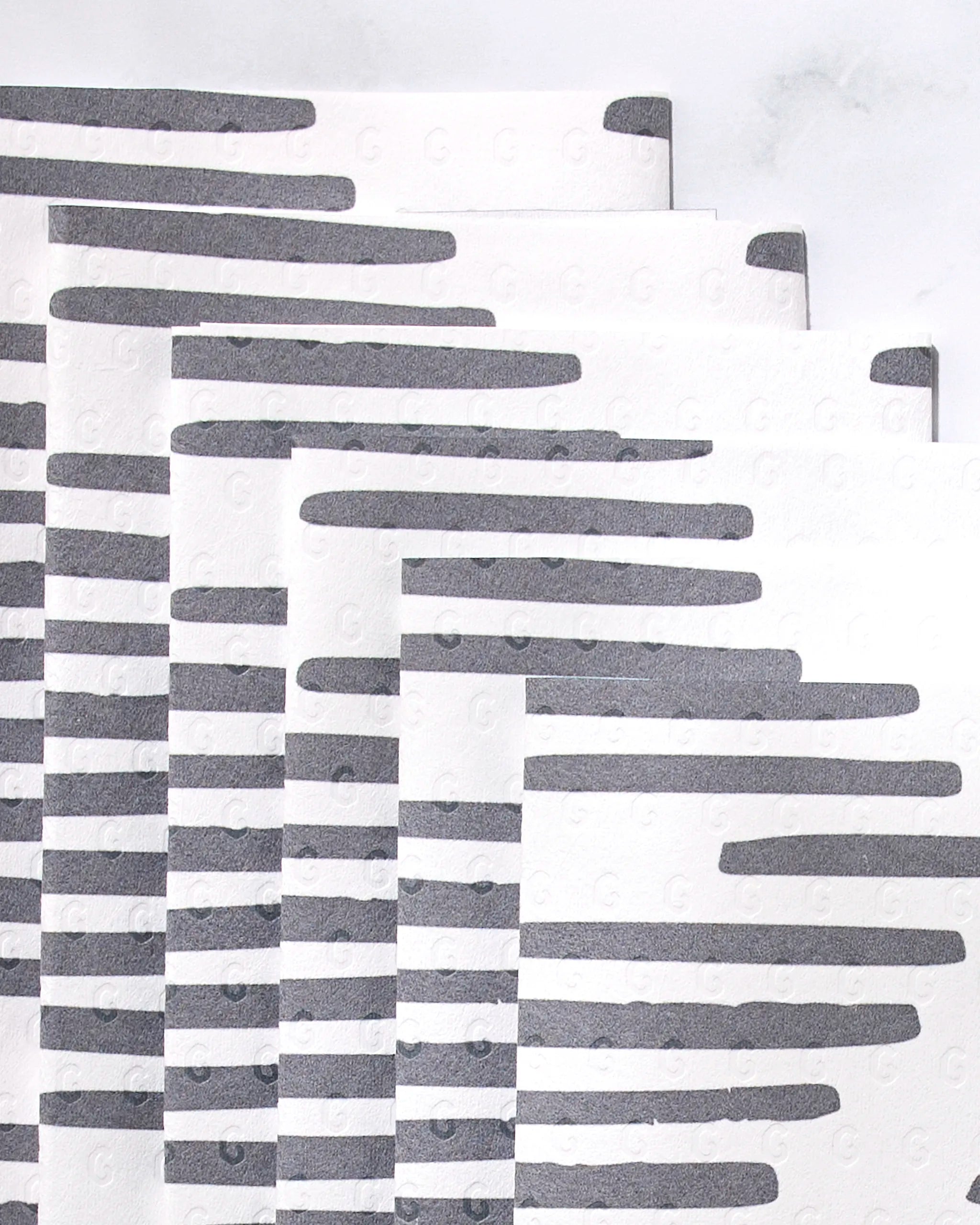Five "Charlie" reusable paper towels by GEOMETRY, featuring bold horizontal black stripes on white, are stacked in a staggered arrangement—a stylish and eco-friendly upgrade for any kitchen.