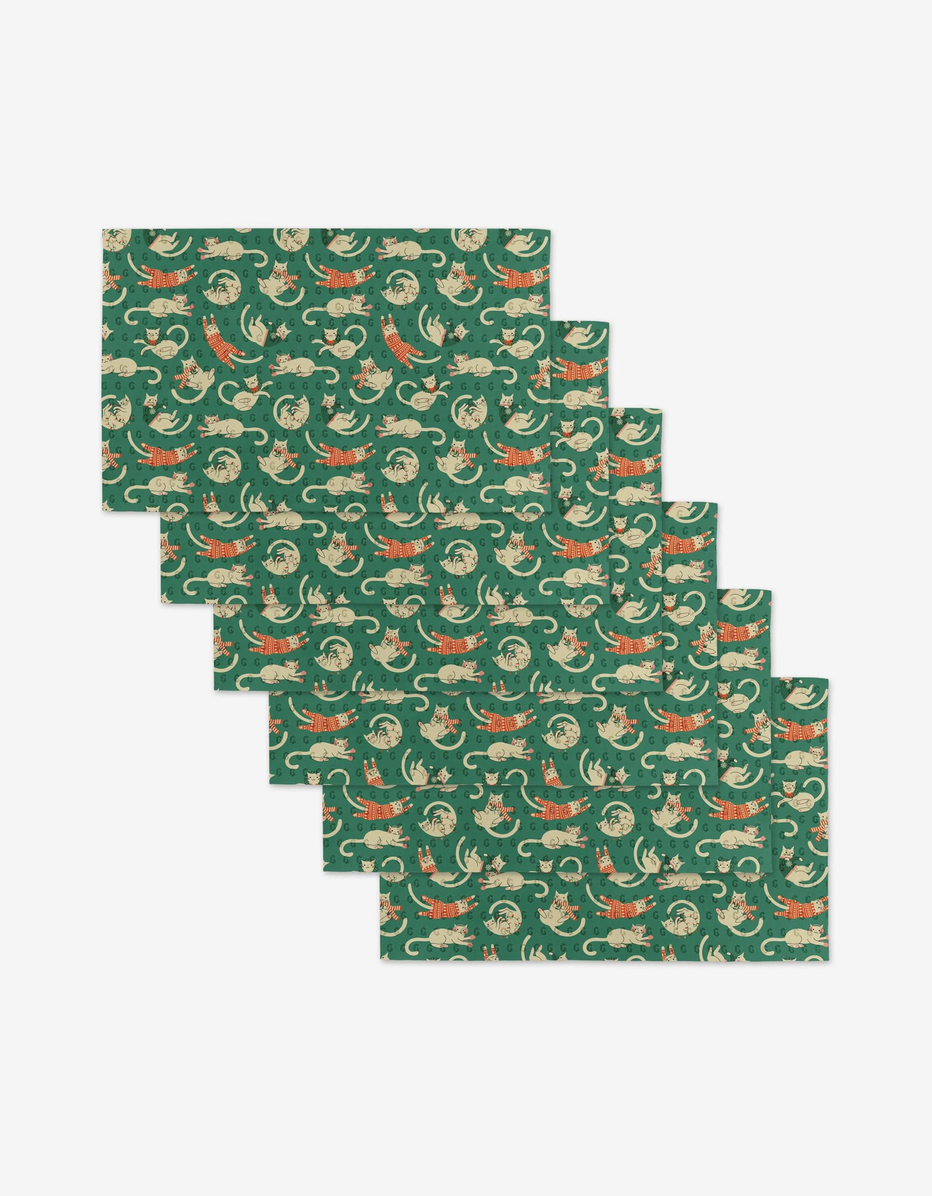 Six rectangular green placemats from Megan Kampa’s Christmas Cats collection are stacked slightly askew, each featuring a repeating pattern of orange cats and light green leaves on a dark green background. Made from eco-friendly materials.